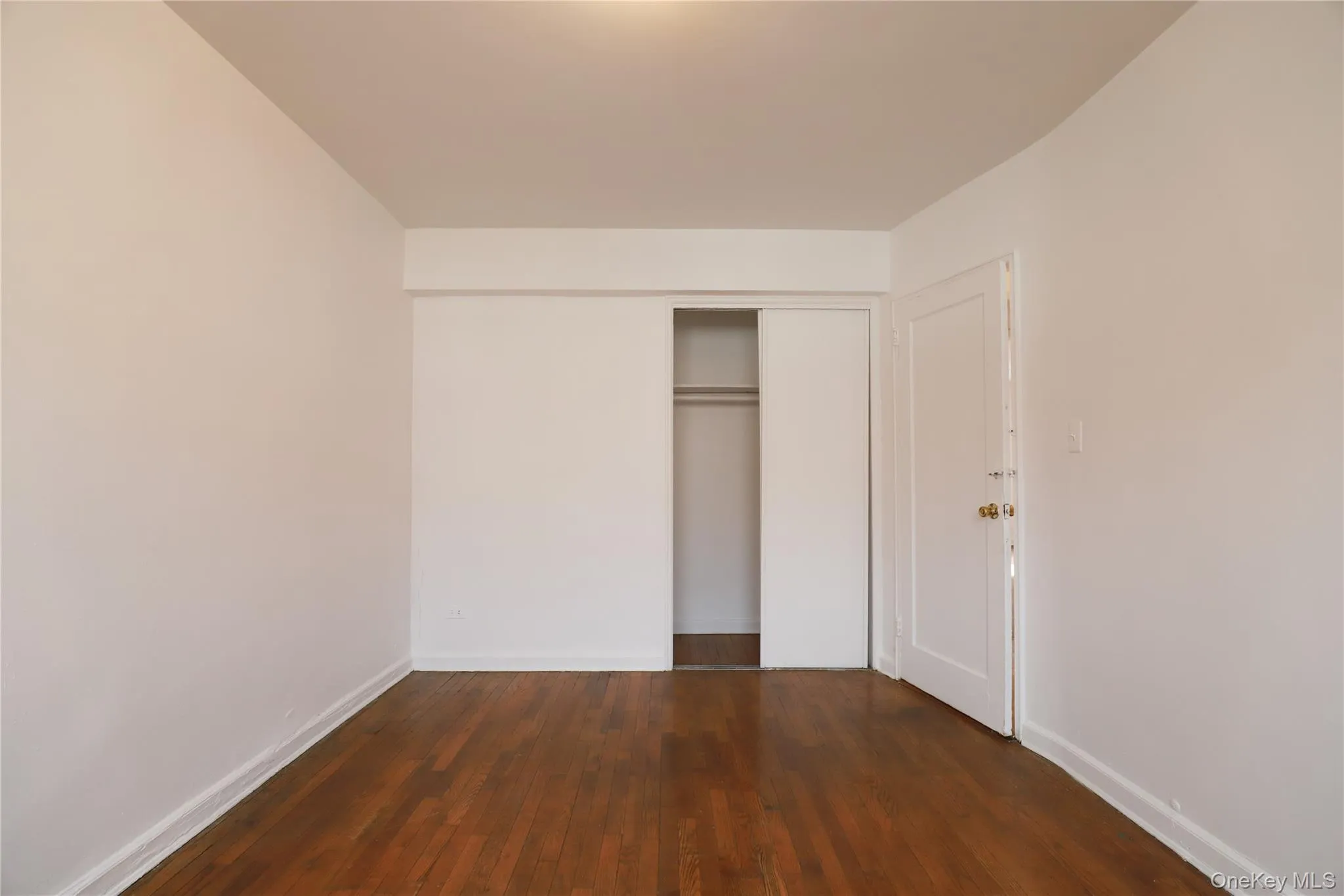 Room featuring wood-finish flooring, white walls, and a recessed ceiling light Room featuring wood-finish flooring, white walls, and a recessed ceiling light