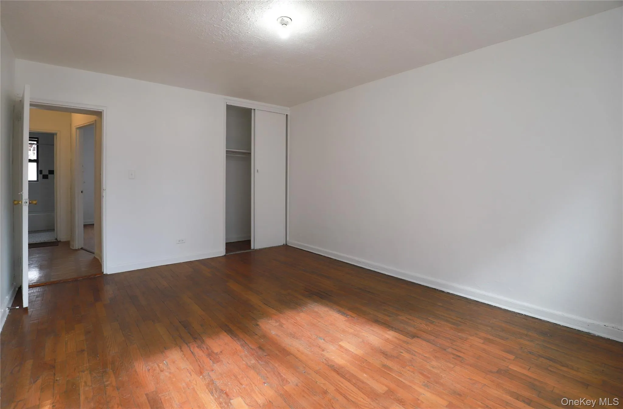 Spacious interior room featuring wood-finish flooring, white painted walls, and a ceiling-mounted light fixture Spacious interior room featuring wood-finish flooring, white painted walls, and a ceiling-mounted light fixture