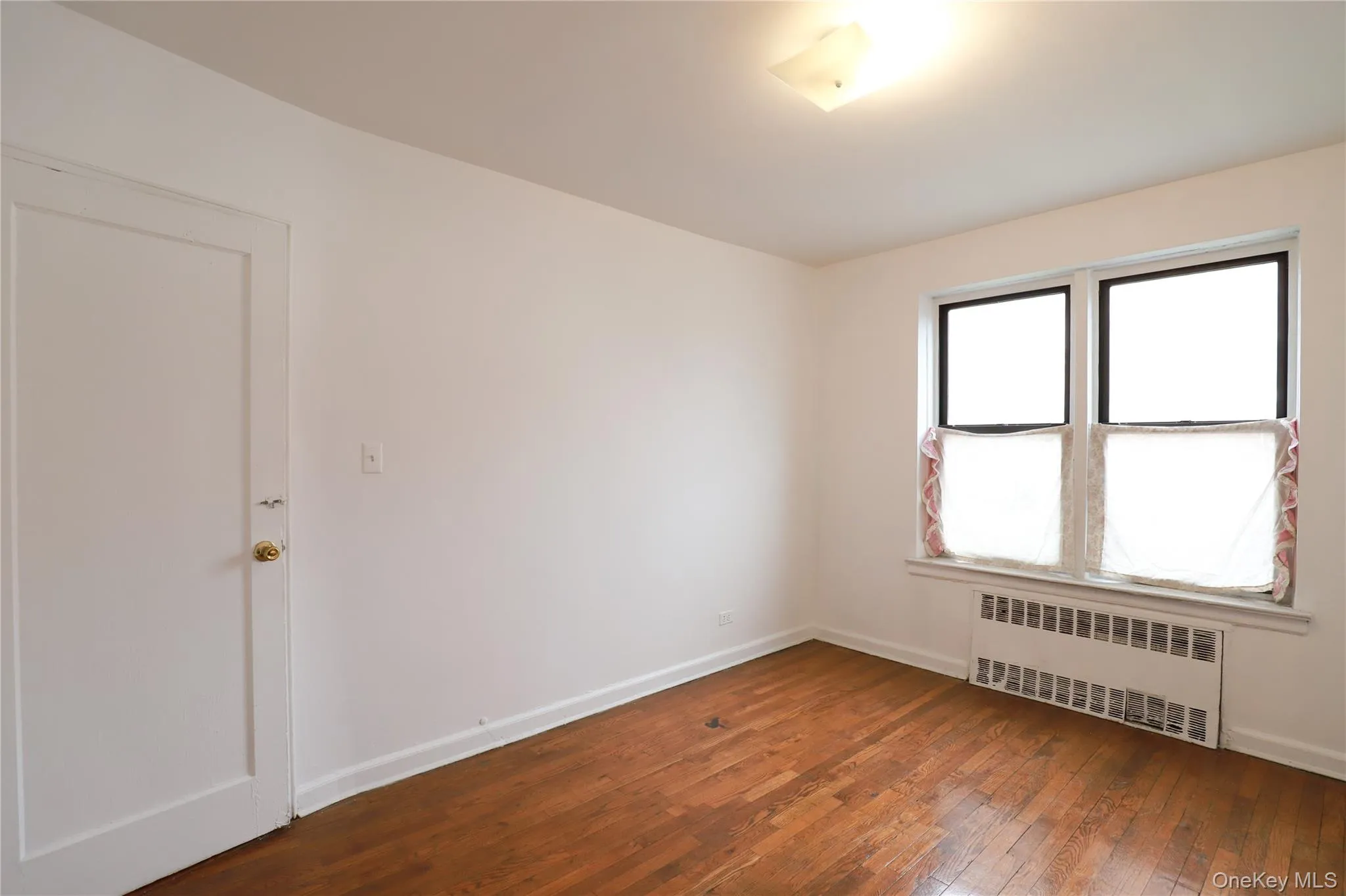 Interior room featuring wood-finish flooring, white walls, and a multi-pane window Interior room featuring wood-finish flooring, white walls, and a multi-pane window