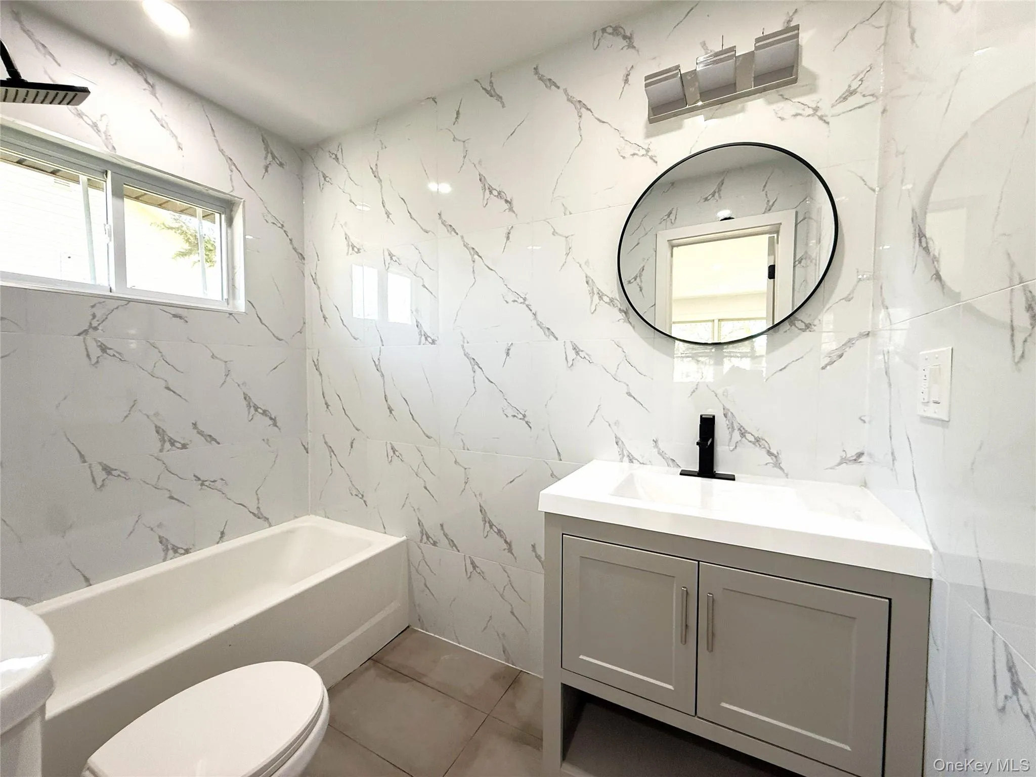 Bathroom featuring white marble-effect wall tiling and a white bathtub Bathroom featuring white marble-effect wall tiling and a white bathtub