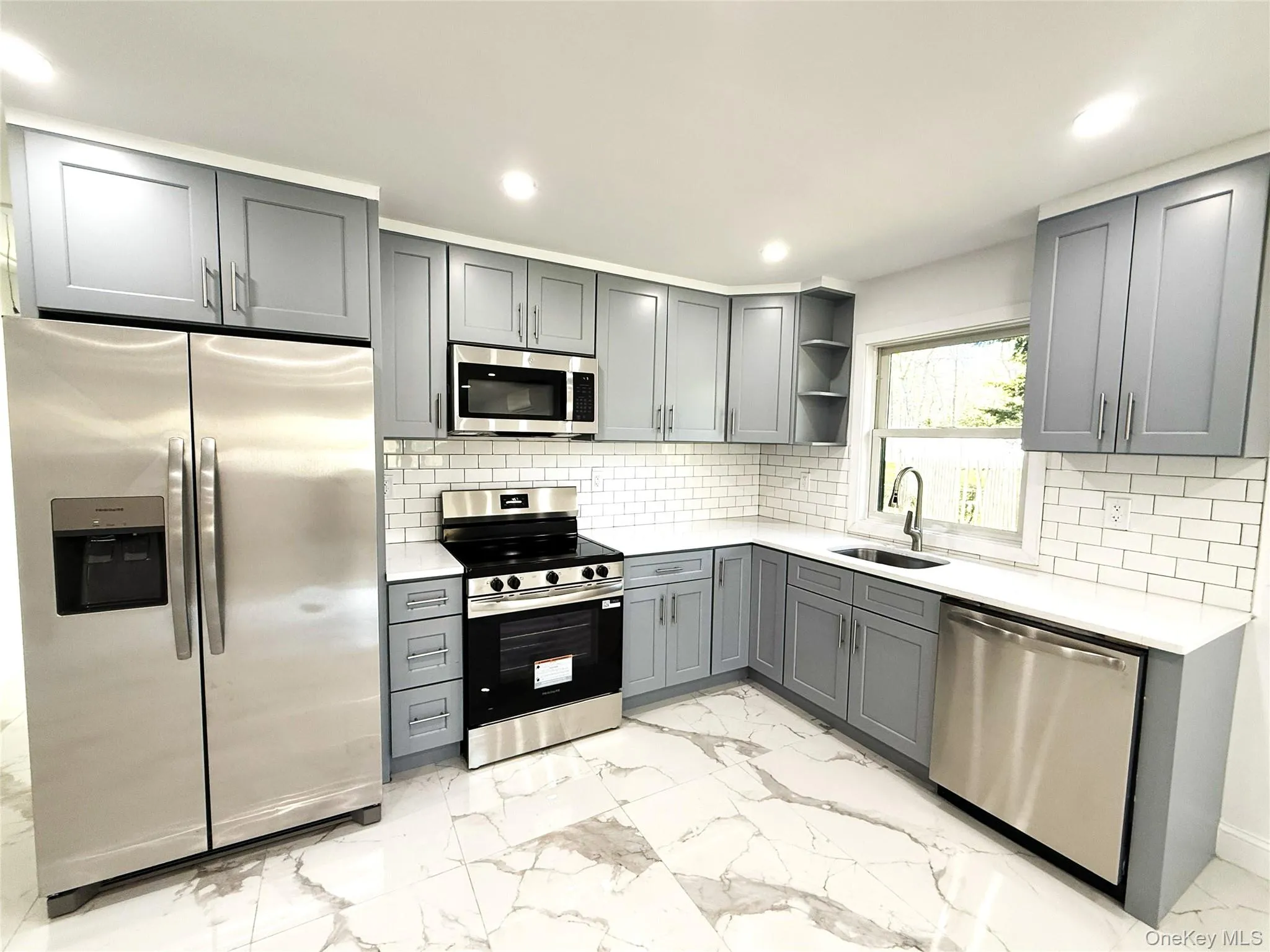 Kitchen featuring gray shaker-style cabinetry, white countertops, subway tile backsplash, stainless steel appliances, and large format marble-look tile flooring Kitchen featuring gray shaker-style cabinetry, white countertops, subway tile backsplash, stainless steel appliances, and large format marble-look tile flooring