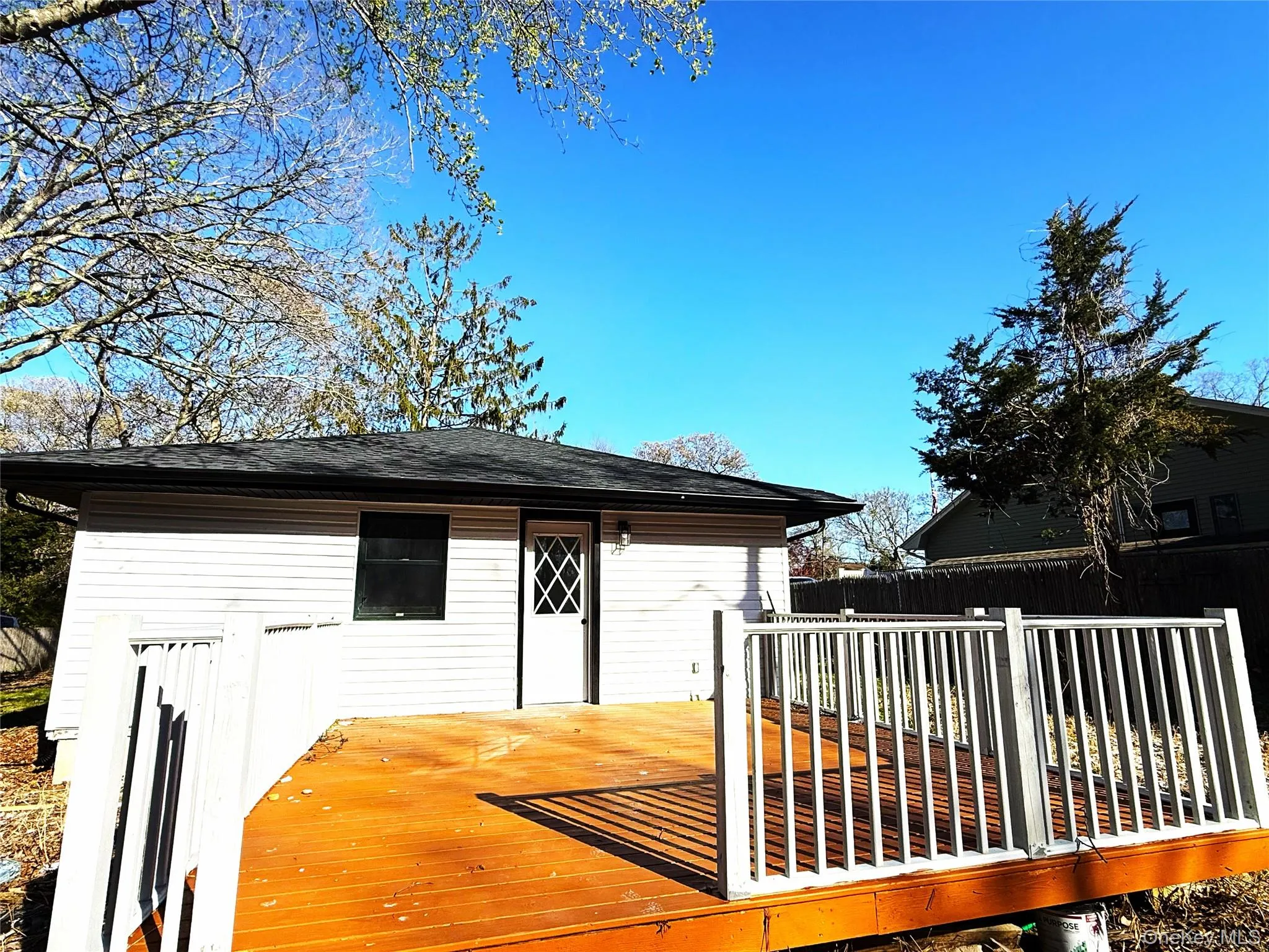 Wood-finish deck with white railings extending from a light-colored siding structure Wood-finish deck with white railings extending from a light-colored siding structure