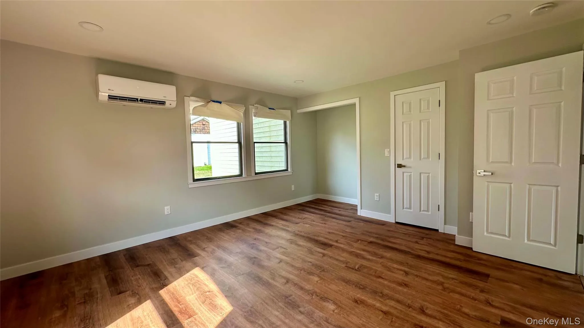 Unfurnished bedroom featuring dark wood-type flooring, a wall mounted air conditioner, and baseboards Unfurnished bedroom featuring dark wood-type flooring, a wall mounted air conditioner, and baseboards