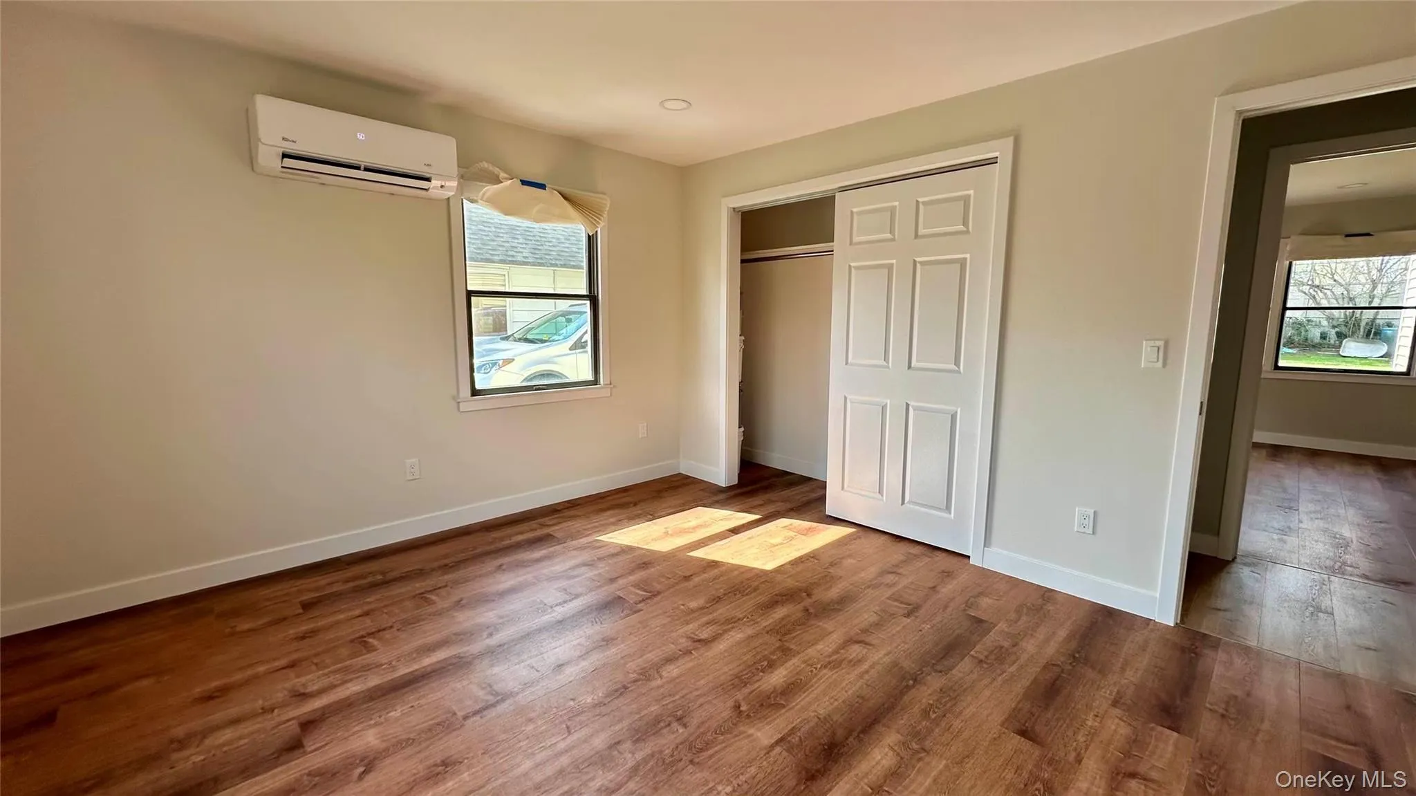 Unfurnished bedroom with wood finished floors, an AC wall unit, baseboards, and multiple windows Unfurnished bedroom with wood finished floors, an AC wall unit, baseboards, and multiple windows