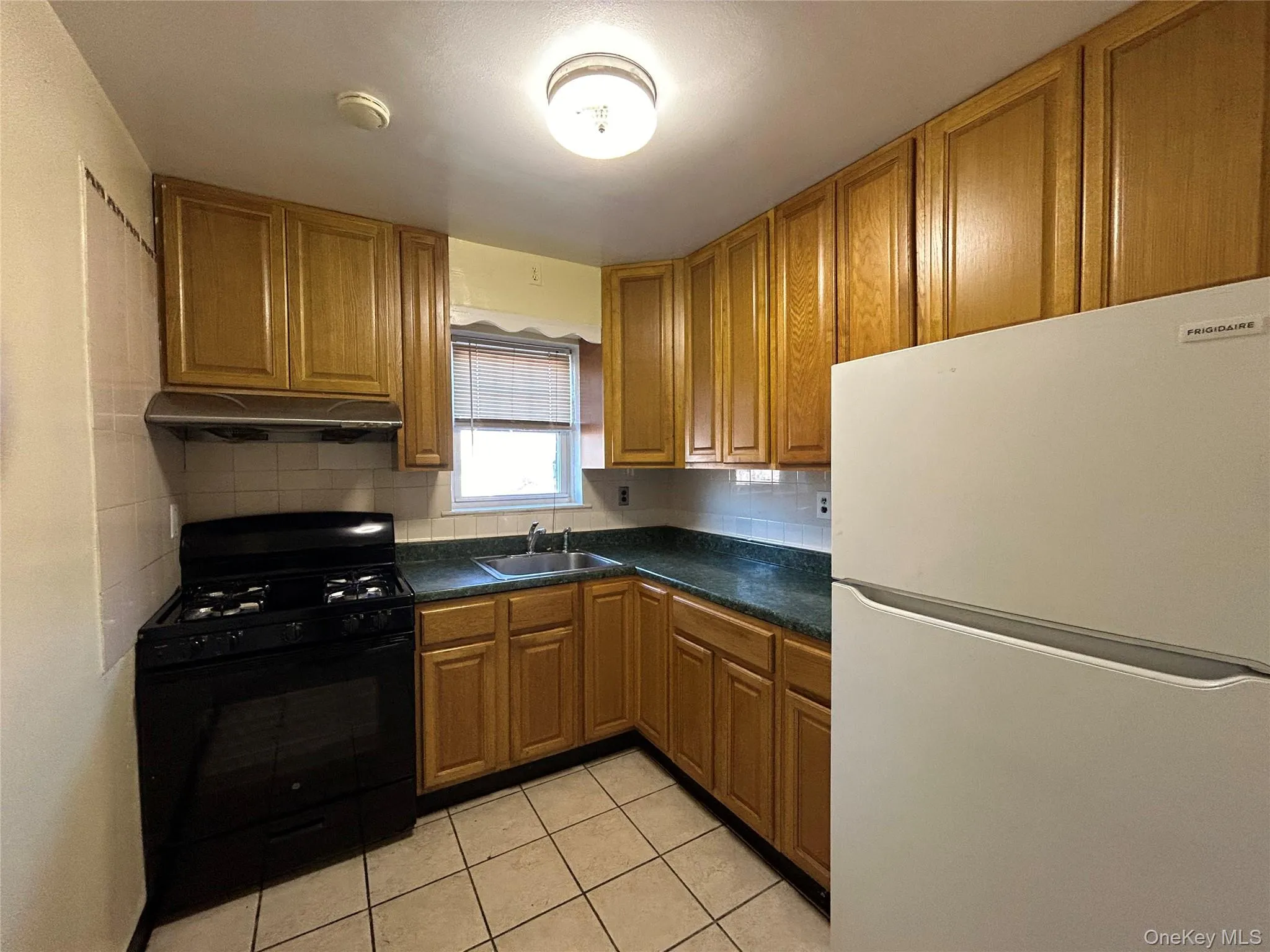 Kitchen with black gas range, dark countertops, freestanding refrigerator, under cabinet range hood, and a sink Kitchen with black gas range, dark countertops, freestanding refrigerator, under cabinet range hood, and a sink