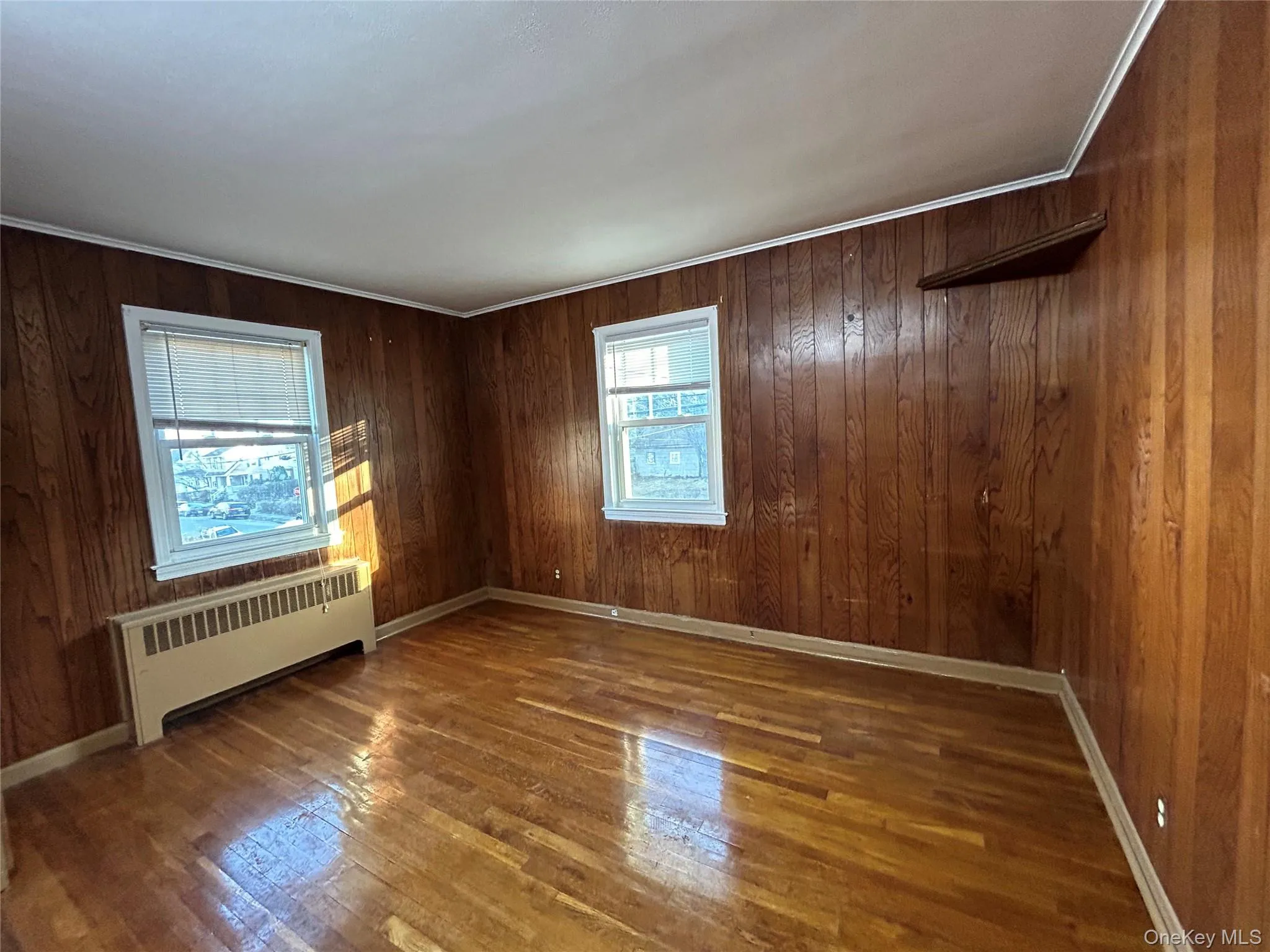 Empty room with ornamental molding, radiator, baseboards, and wood finished floors Empty room with ornamental molding, radiator, baseboards, and wood finished floors