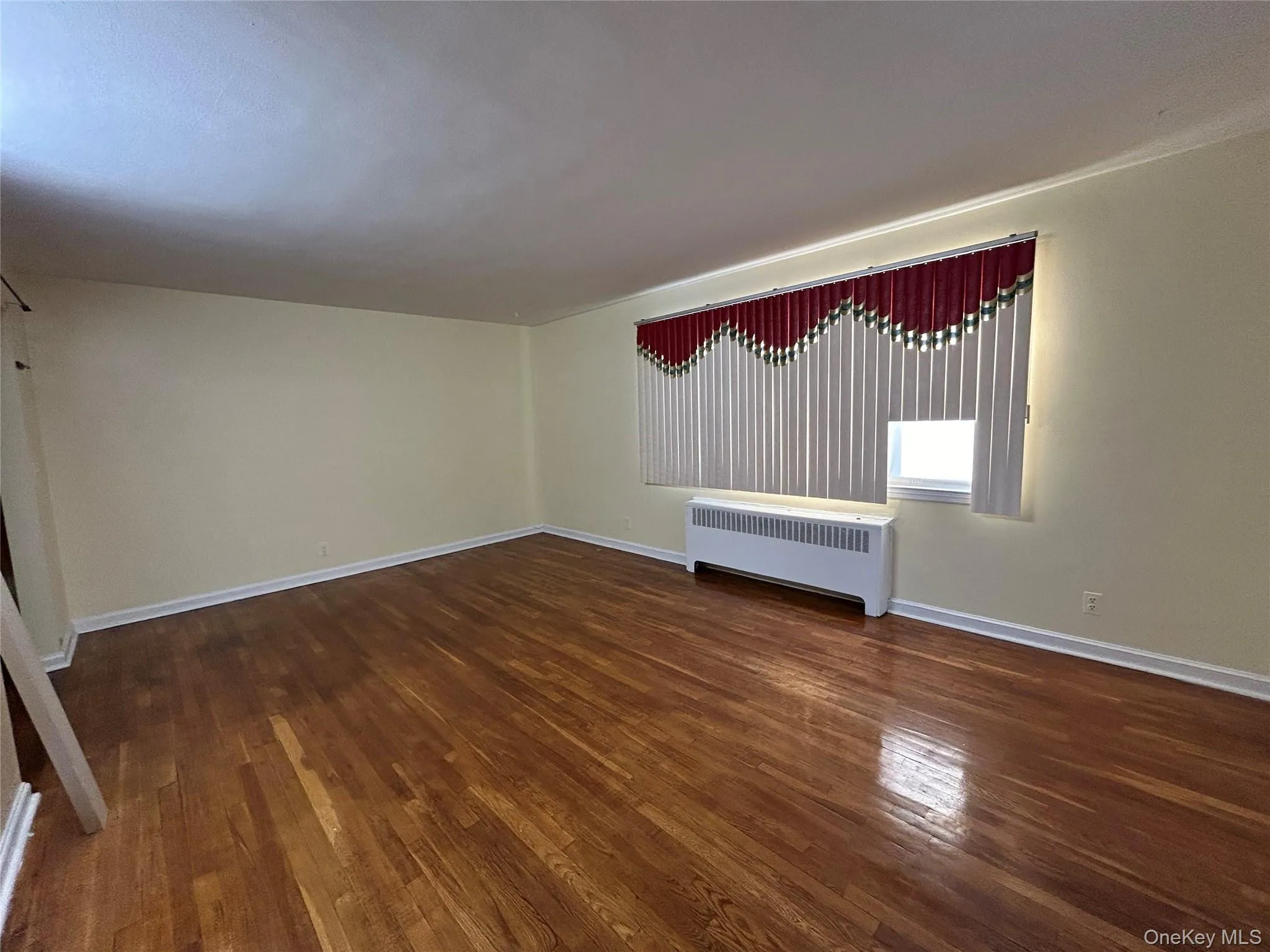 Unfurnished room with radiator, baseboards, and hardwood / wood-style floors Unfurnished room with radiator, baseboards, and hardwood / wood-style floors