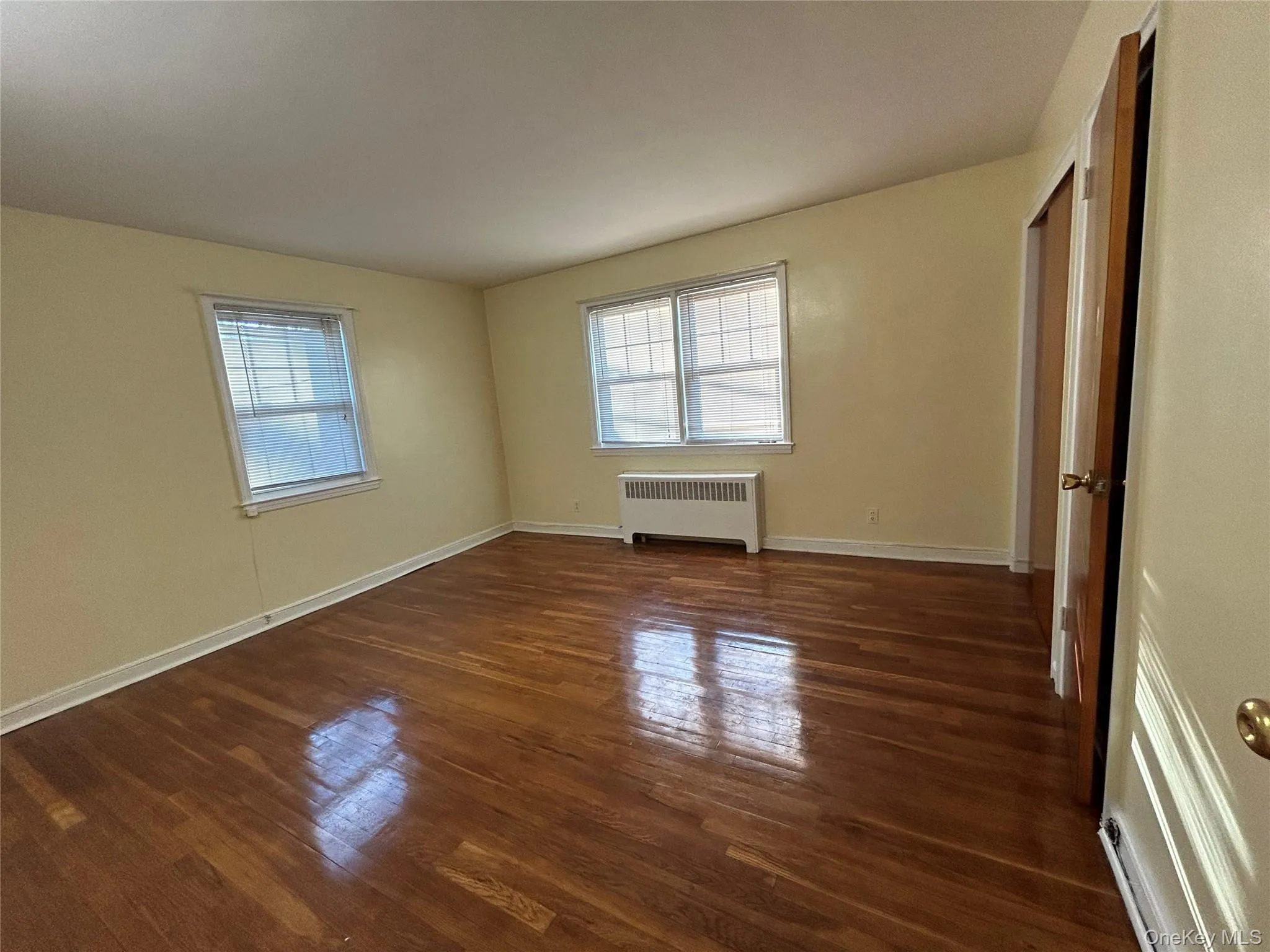 Empty room with baseboards, a healthy amount of sunlight, radiator heating unit, and wood finished floors Empty room with baseboards, a healthy amount of sunlight, radiator heating unit, and wood finished floors