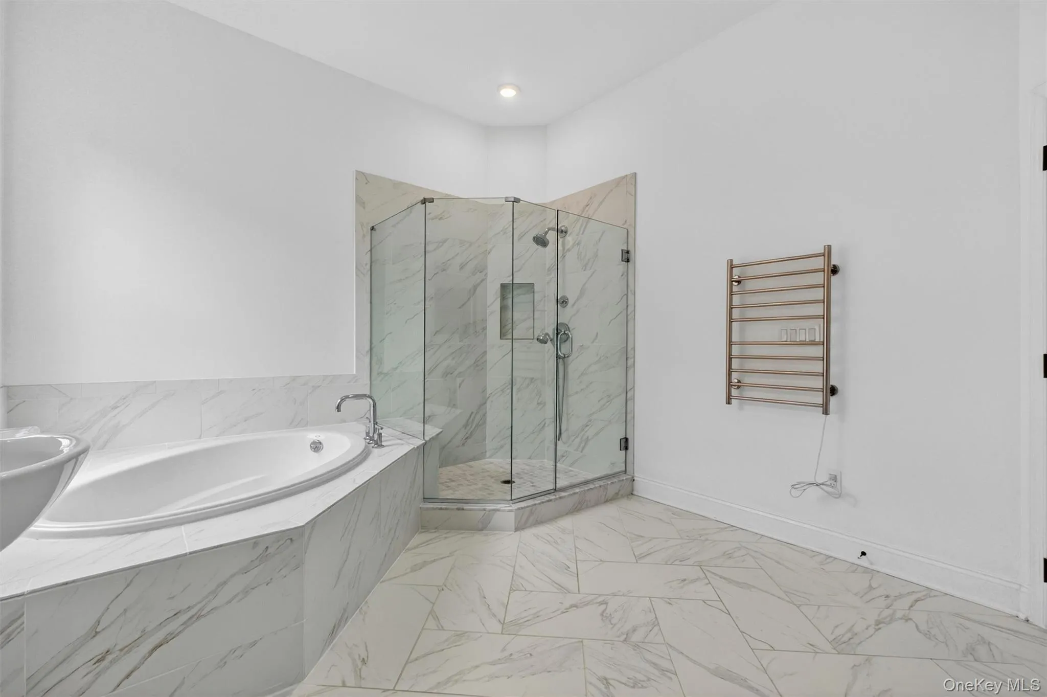 Primary bathroom featuring a corner glass-enclosed shower, a large soaking tub with deck-mounted fixtures, and a wall-mounted towel warmer Primary bathroom featuring a corner glass-enclosed shower, a large soaking tub with deck-mounted fixtures, and a wall-mounted towel warmer