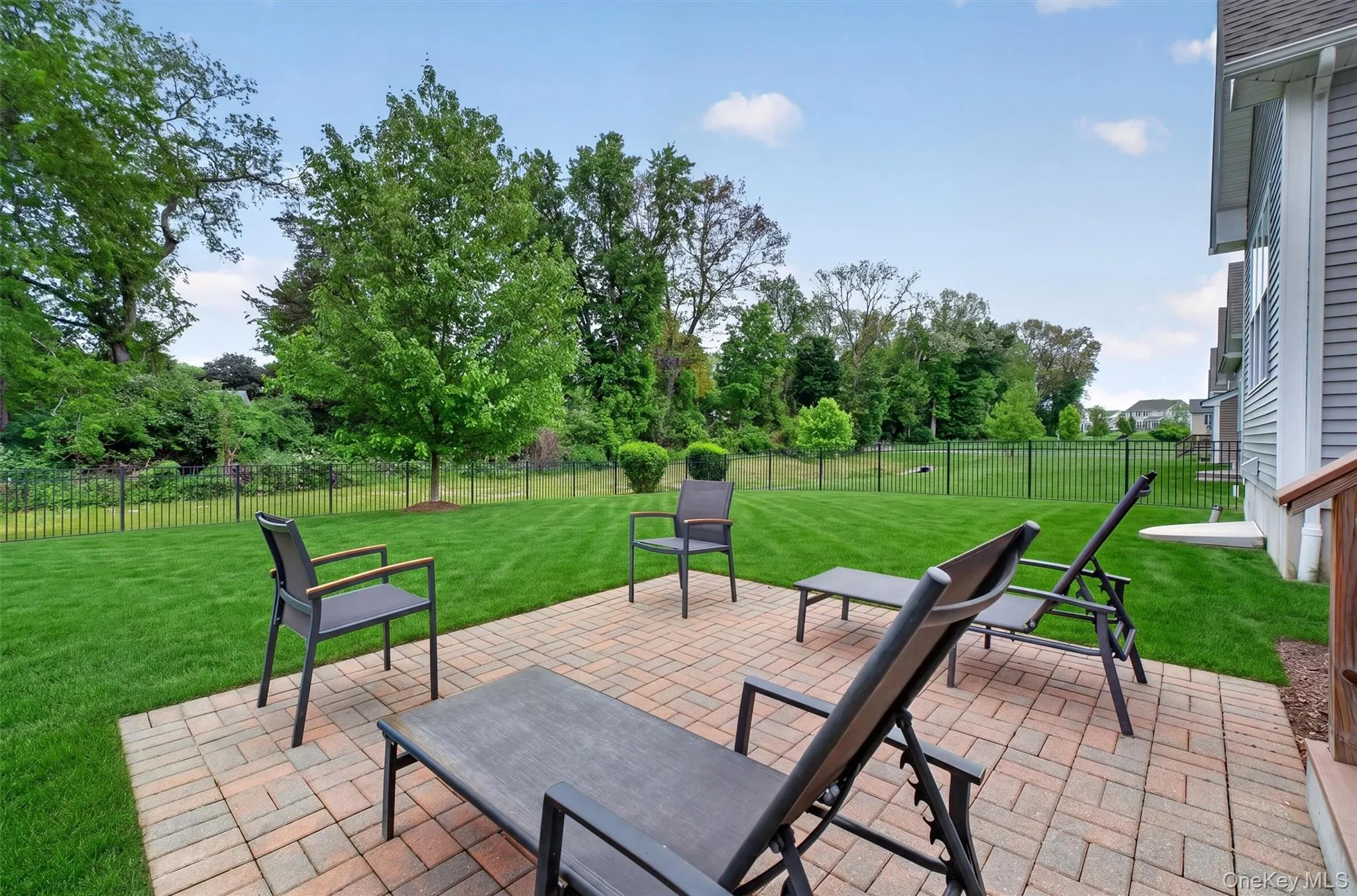 Expansive lawn with a paver patio and a black metal fence Expansive lawn with a paver patio and a black metal fence