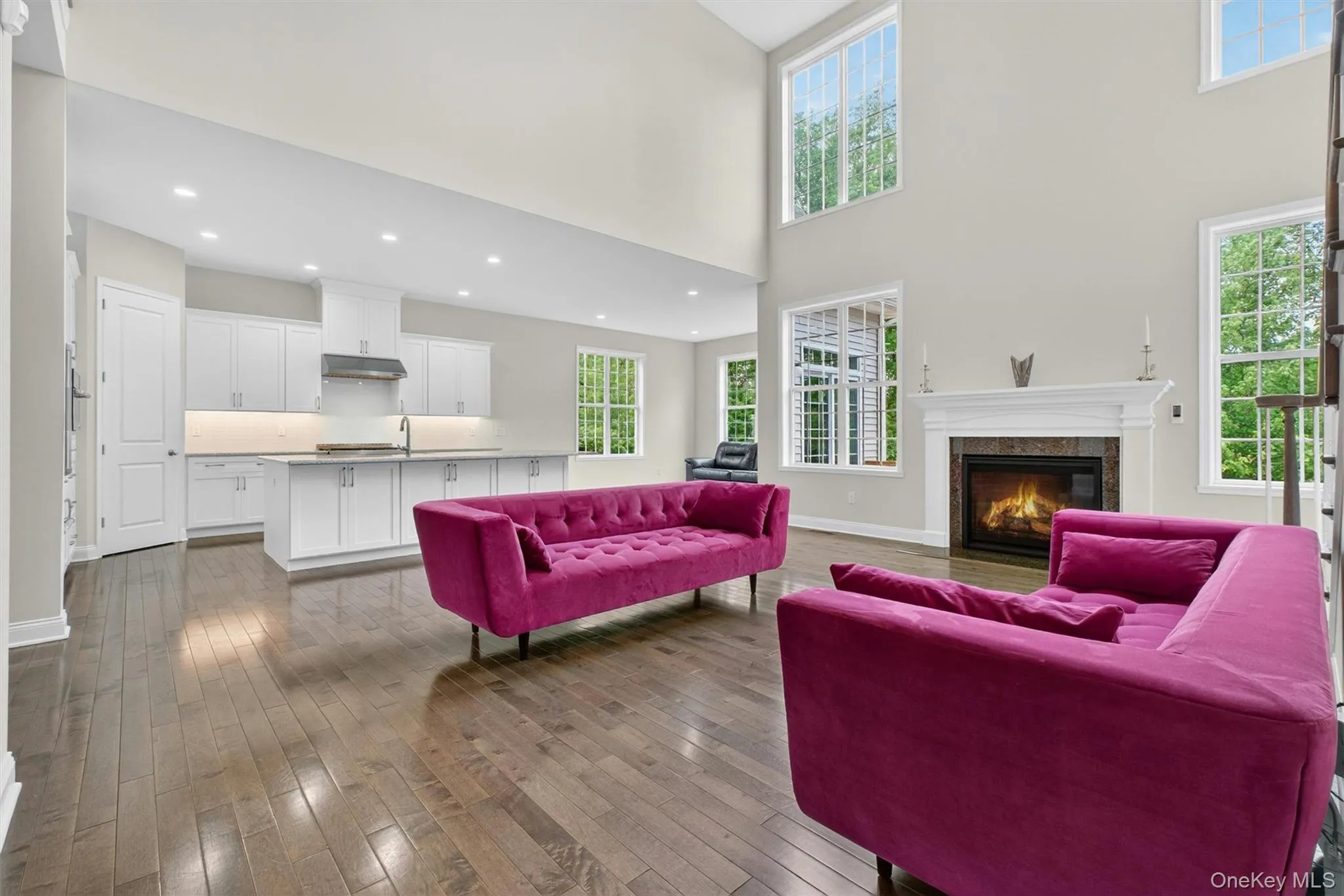 Expansive living area with wood-finish flooring and a stone surround fireplace with a white mantel Expansive living area with wood-finish flooring and a stone surround fireplace with a white mantel