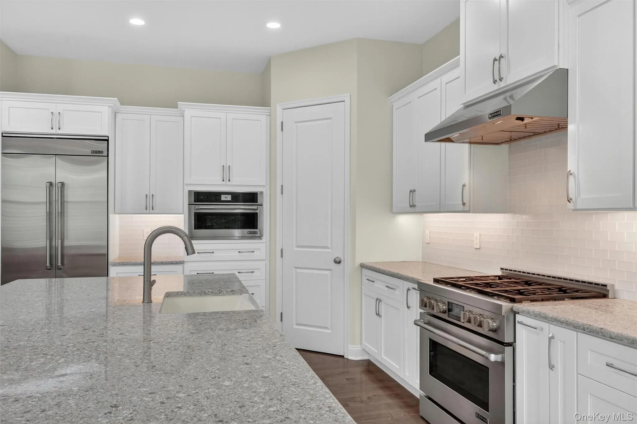 Kitchen featuring a large island with an undermount sink, stainless steel appliances, white shaker cabinetry, tiled backsplash, and recessed lighting Kitchen featuring a large island with an undermount sink, stainless steel appliances, white shaker cabinetry, tiled backsplash, and recessed lighting