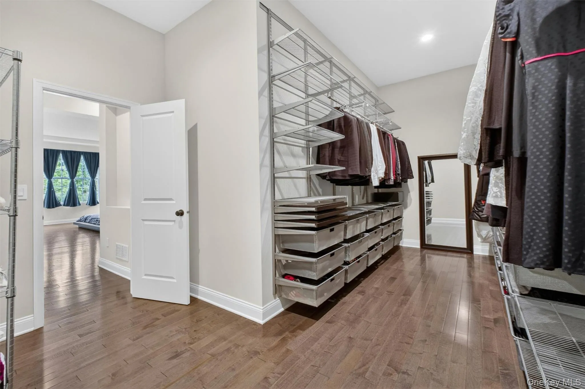 Primary Bedroom Walk-in closet featuring wood-finish flooring, white baseboards, and built-in metal shelving with integrated drawers Primary Bedroom Walk-in closet featuring wood-finish flooring, white baseboards, and built-in metal shelving with integrated drawers