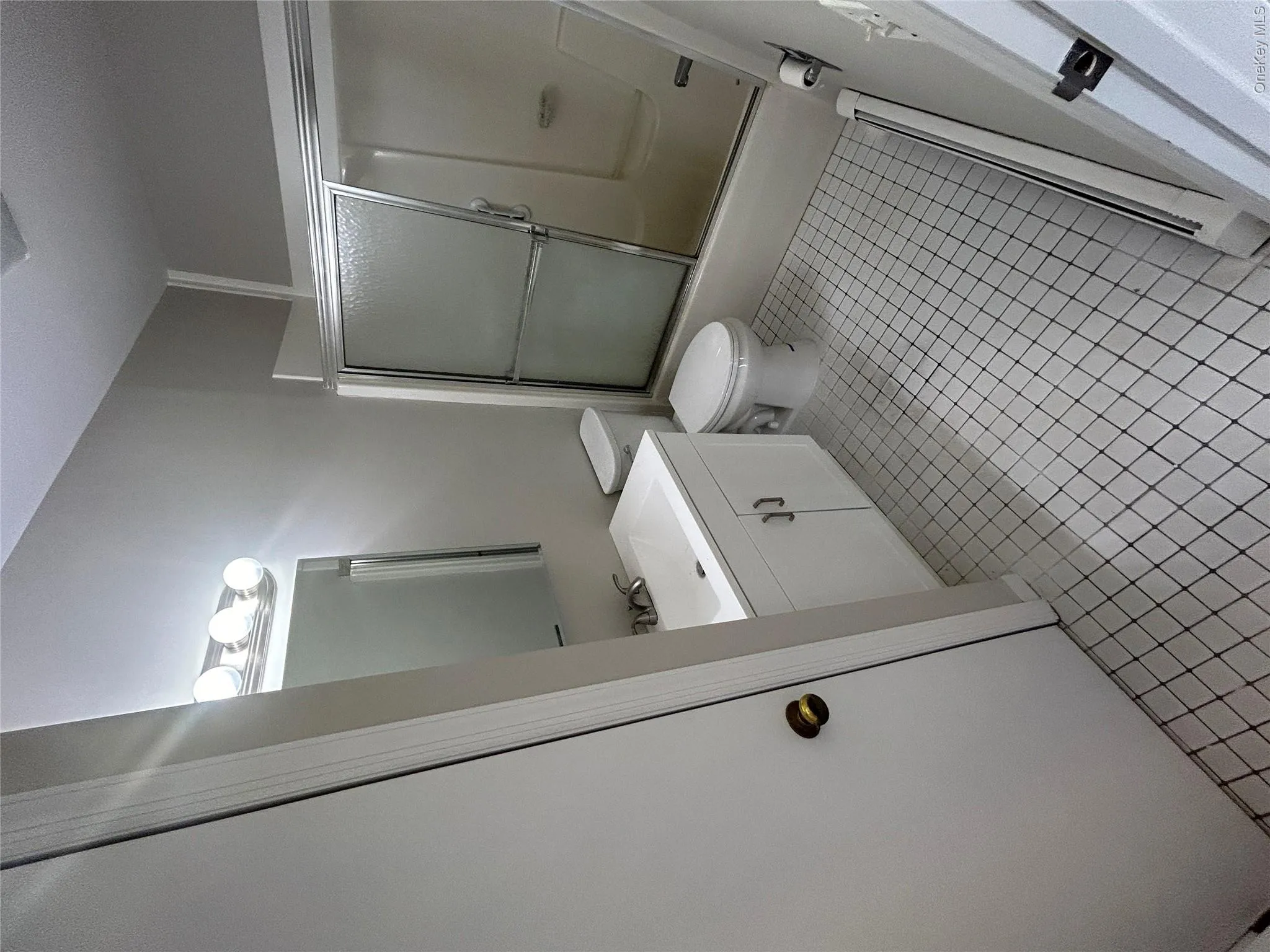 Bathroom featuring diamond pattern floor tiling, white vanity with integrated sink, chrome faucet, and a shower-tub combination with sliding glass doors Bathroom featuring diamond pattern floor tiling, white vanity with integrated sink, chrome faucet, and a shower-tub combination with sliding glass doors