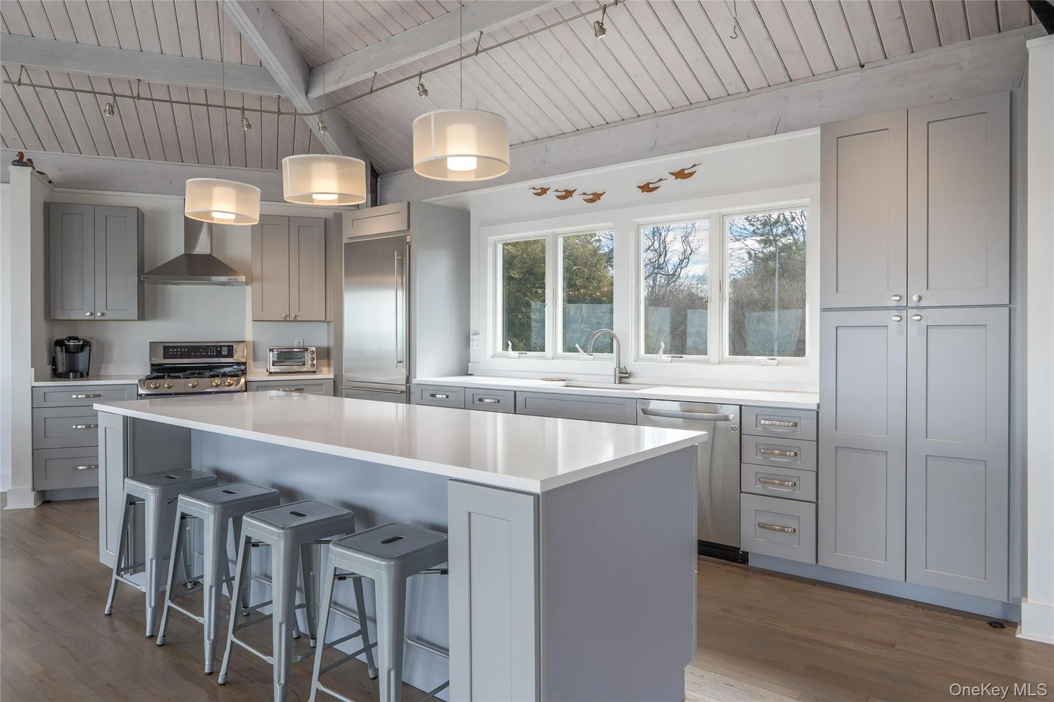 Kitchen with a sink, wall chimney range hood, stainless steel appliances, and gray cabinets Kitchen with a sink, wall chimney range hood, stainless steel appliances, and gray cabinets