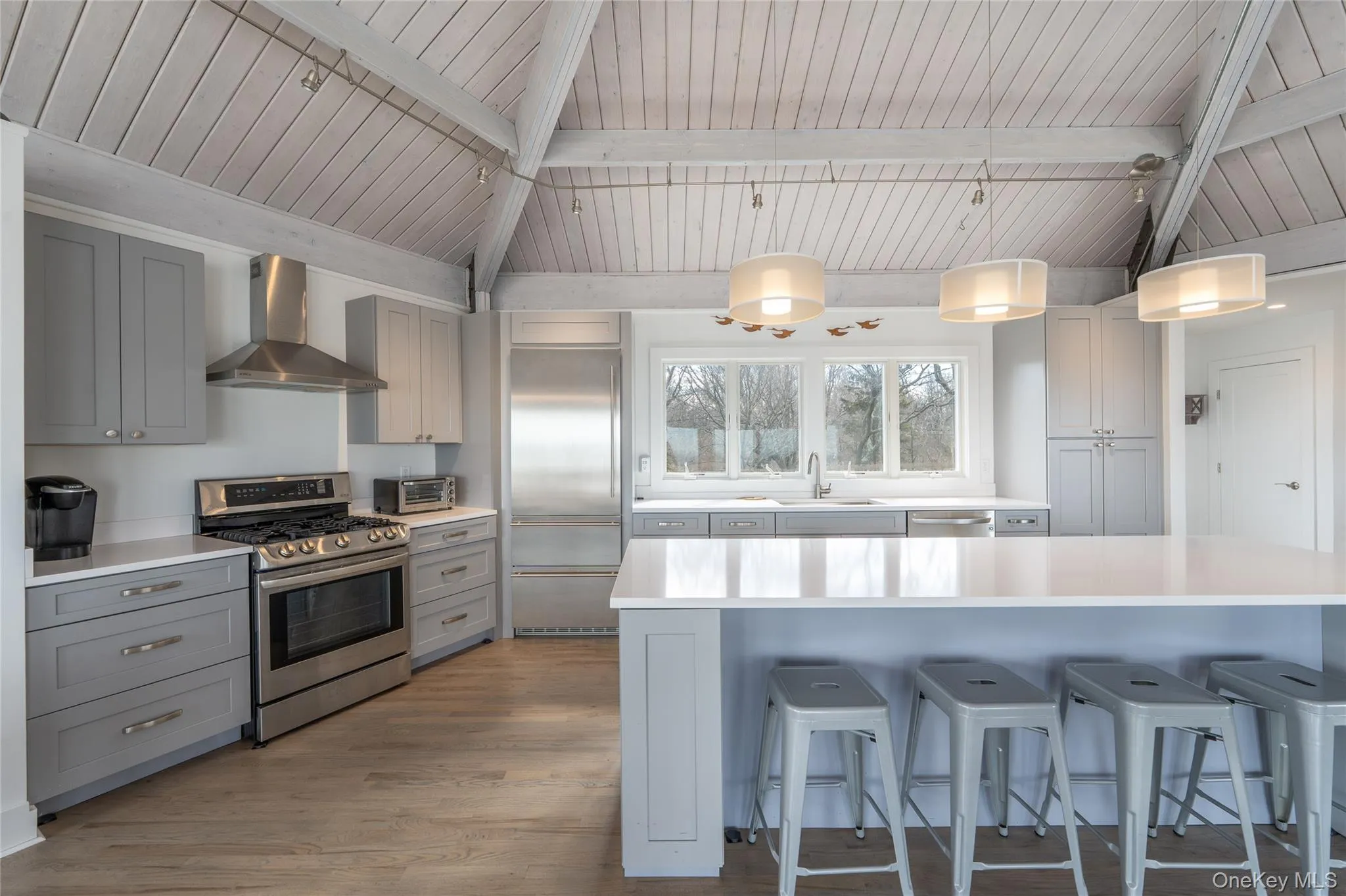 Kitchen featuring wood finished floors, stainless steel appliances, a sink, wall chimney range hood, and gray cabinets Kitchen featuring wood finished floors, stainless steel appliances, a sink, wall chimney range hood, and gray cabinets