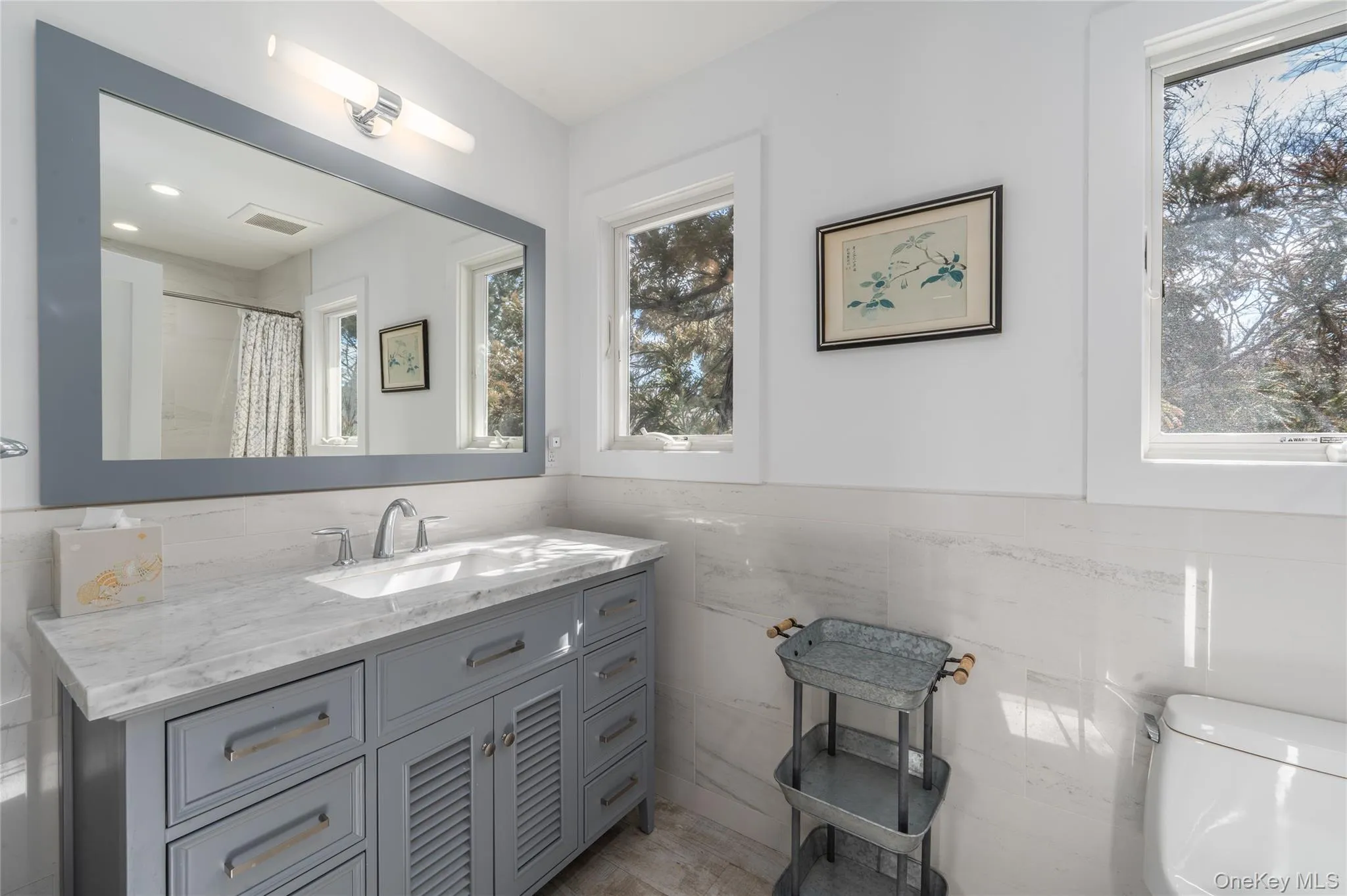 Bathroom featuring tile walls, visible vents, toilet, vanity, and wainscoting Bathroom featuring tile walls, visible vents, toilet, vanity, and wainscoting