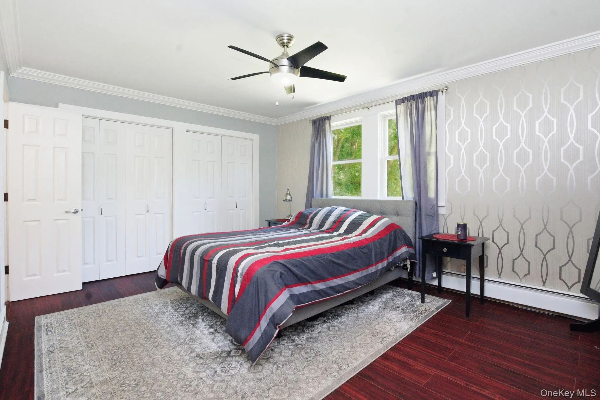 A spacious primary bedroom with rich flooring, custom crown molding, and generous double closets, overlooking spacious backyard and pond. A spacious primary bedroom with rich flooring, custom crown molding, and generous double closets, overlooking spacious backyard and pond.