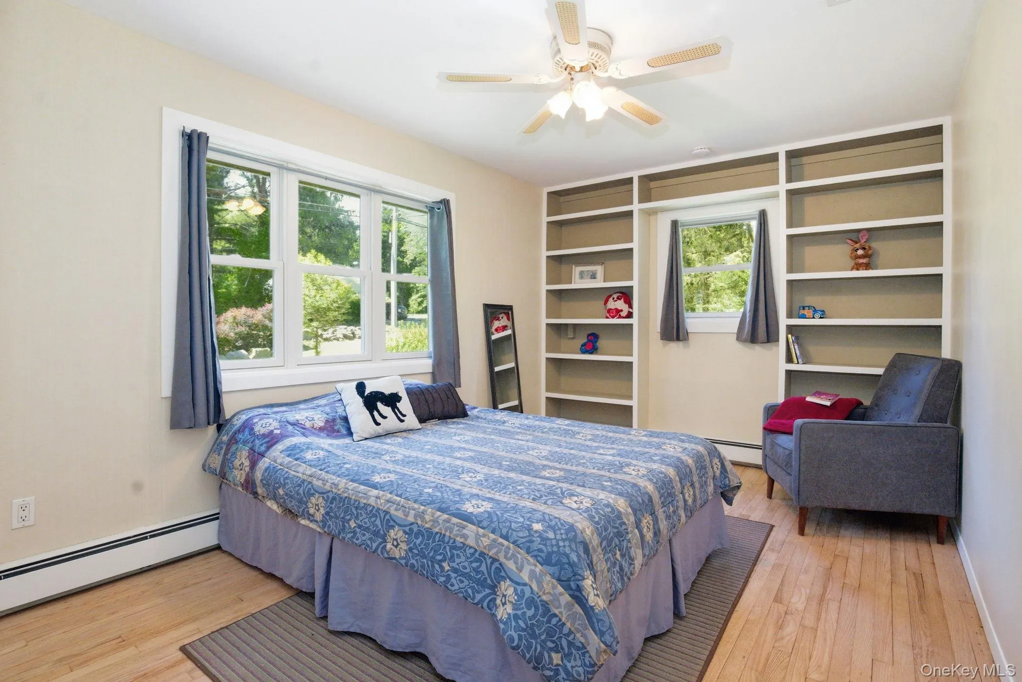 A bright, generously sized bedroom with hardwood floors and handsome built-in shelving framing the windows. A bright, generously sized bedroom with hardwood floors and handsome built-in shelving framing the windows.