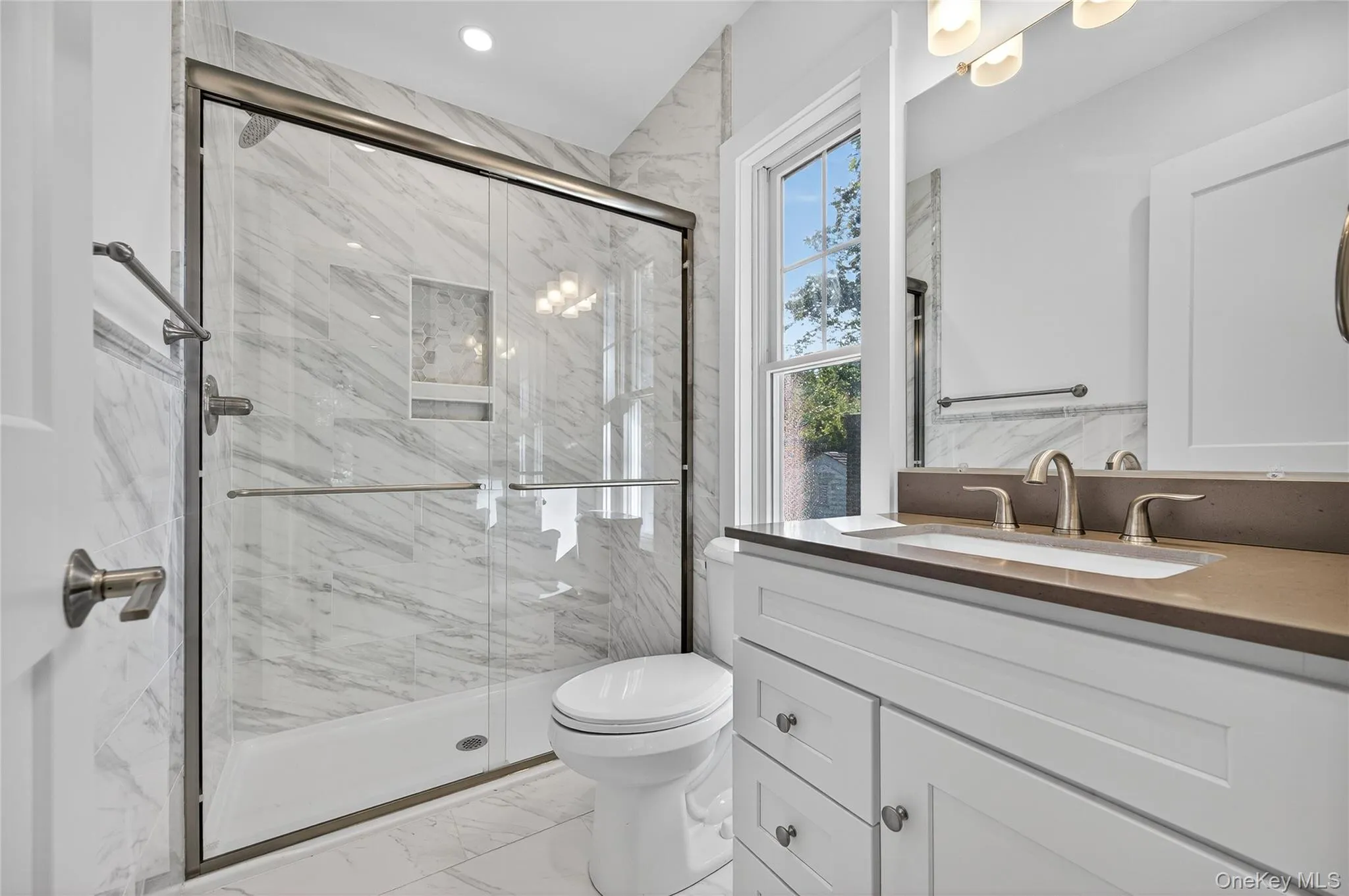 Bathroom featuring light marble finish floors, a marble finish shower, and vanity Bathroom featuring light marble finish floors, a marble finish shower, and vanity