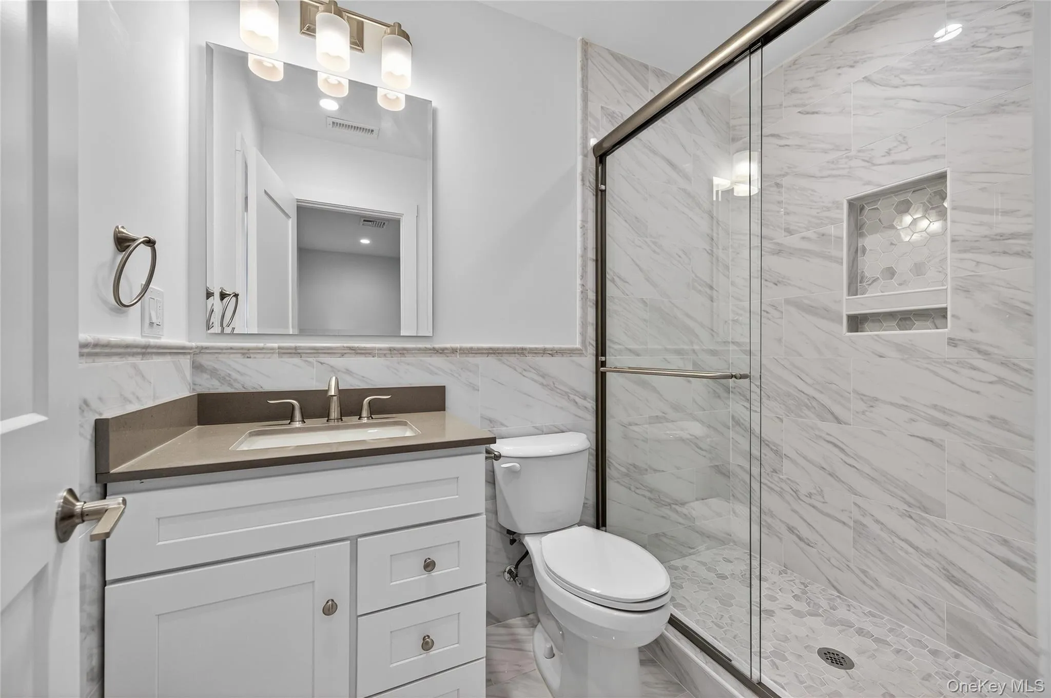 Bathroom with a marble finish shower, vanity, and tile walls Bathroom with a marble finish shower, vanity, and tile walls