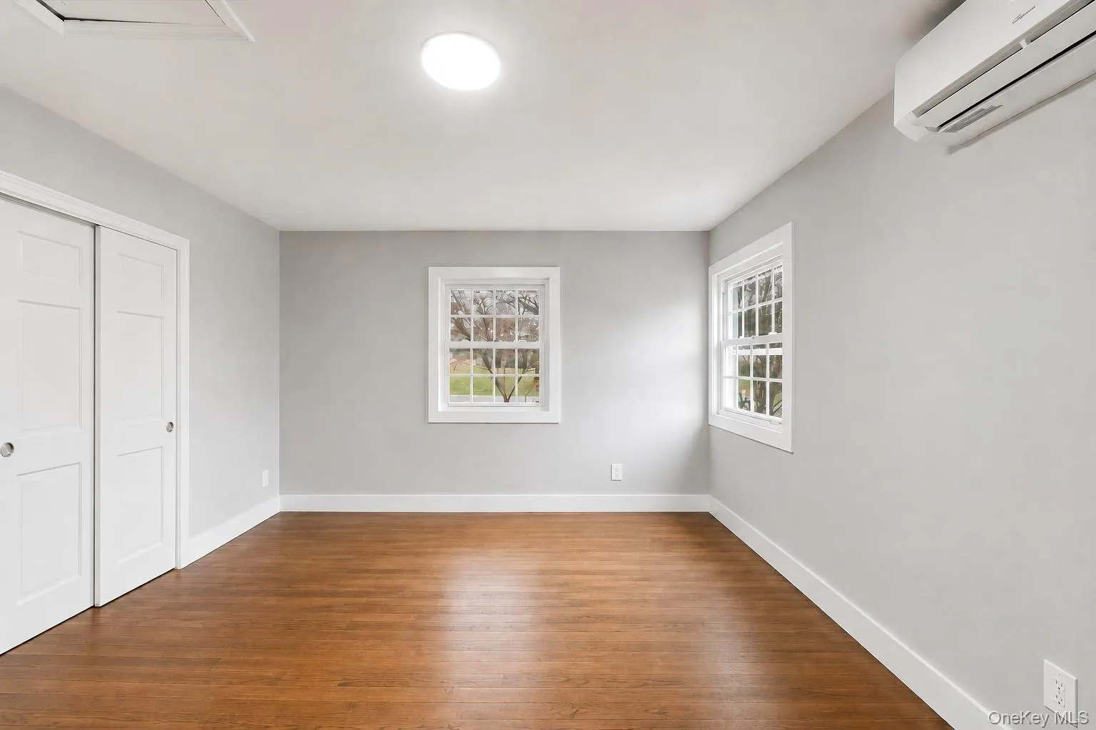 Light-filled 2nd bedroom featuring wood-finish flooring, two large windows, and a round overhead light fixture Light-filled 2nd bedroom featuring wood-finish flooring, two large windows, and a round overhead light fixture