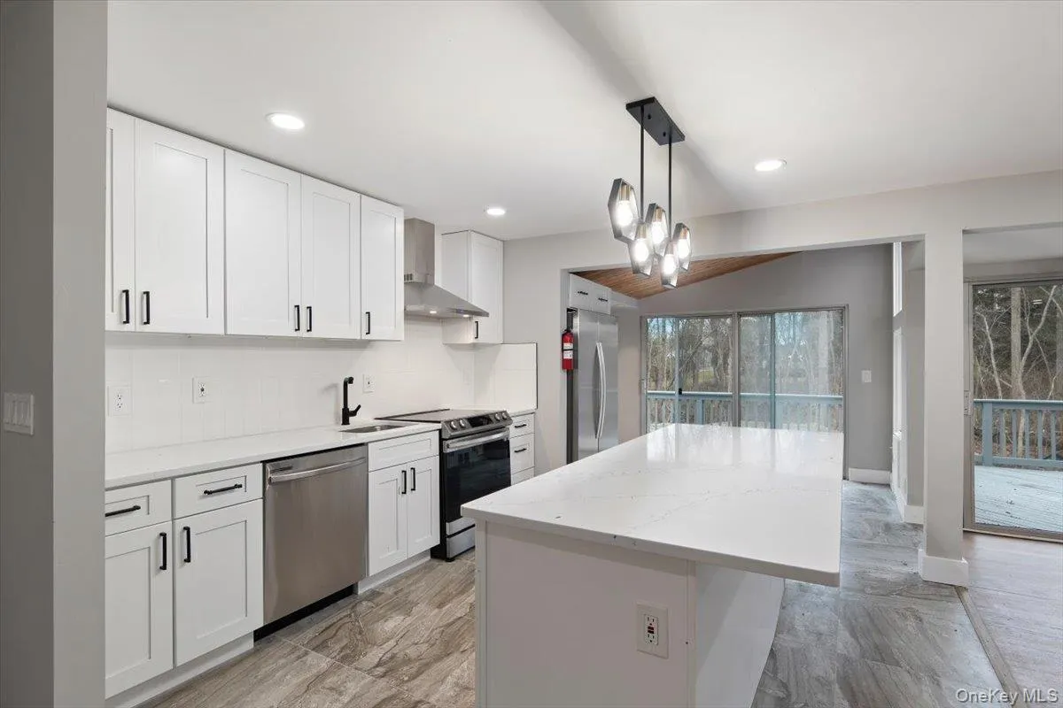 Modern kitchen featuring white shaker cabinetry, stainless steel appliances, quartz countertops, and a full tile backsplash Modern kitchen featuring white shaker cabinetry, stainless steel appliances, quartz countertops, and a full tile backsplash