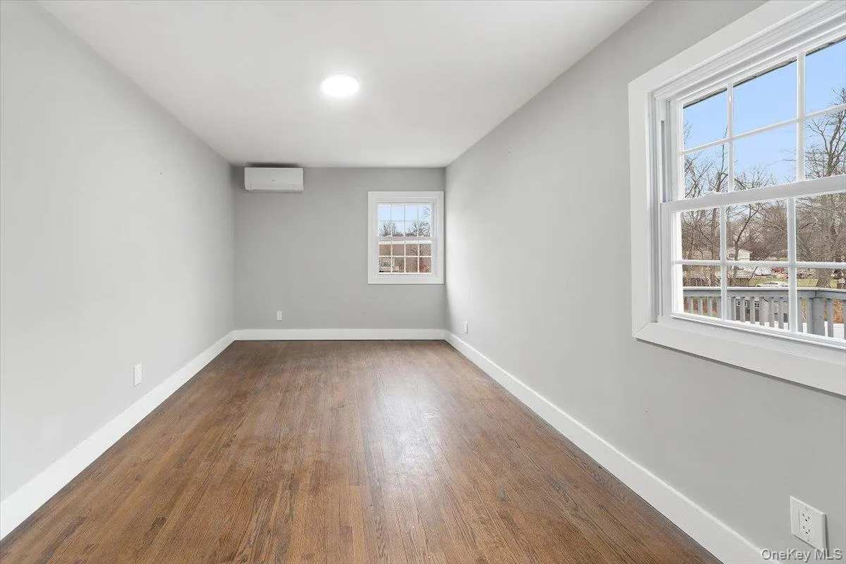 Spacious Primary Bedroom (main floor) featuring wood-finish flooring, light gray walls, white trim, and two windows with multi-pane sashes Spacious Primary Bedroom (main floor) featuring wood-finish flooring, light gray walls, white trim, and two windows with multi-pane sashes