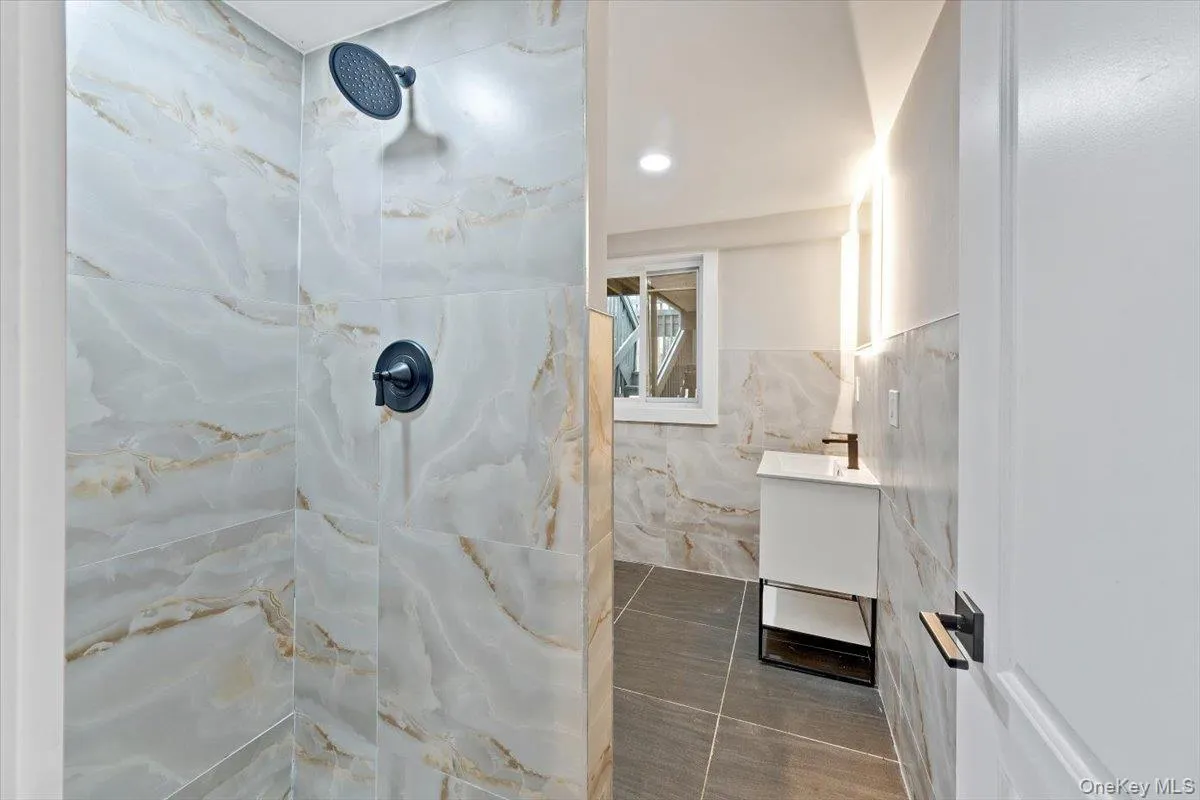 Full Bathroom featuring (basement) a tiled shower with a rain-style showerhead and matte black fixtures Full Bathroom featuring (basement) a tiled shower with a rain-style showerhead and matte black fixtures