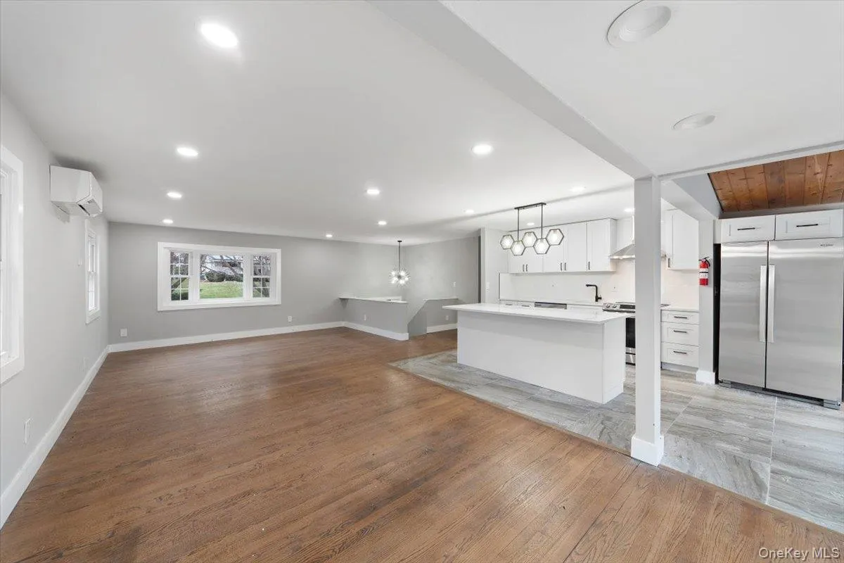 Expansive open-concept living area featuring wood-finish flooring, recessed lighting, and a modern kitchen Expansive open-concept living area featuring wood-finish flooring, recessed lighting, and a modern kitchen