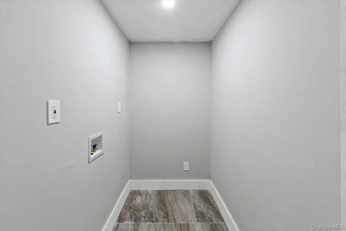 Laundry room (basement) featuring wood-finish tile flooring, light gray wall paint, and white baseboards; washer and dryer hook up. Laundry room (basement) featuring wood-finish tile flooring, light gray wall paint, and white baseboards; washer and dryer hook up.