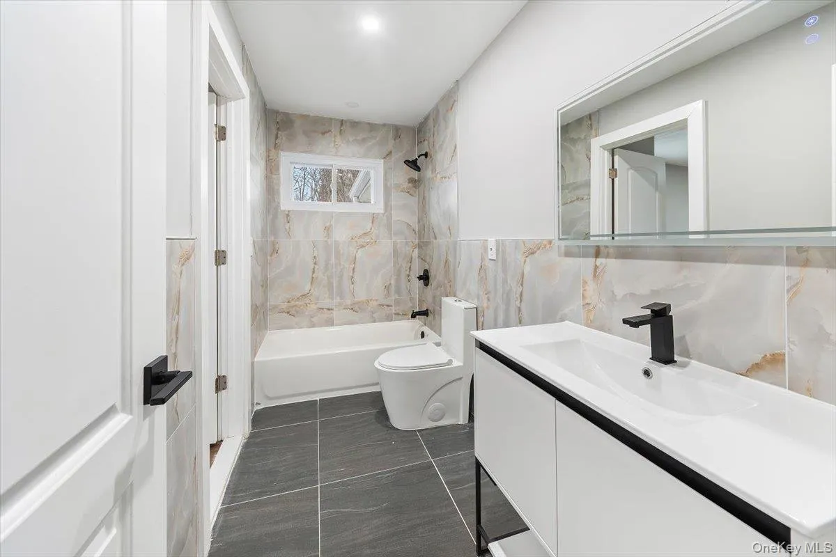 Bathroom with a contemporary vanity, black fixtures, tiled floor, a bathtub with a tiled surround, and a compact window Bathroom with a contemporary vanity, black fixtures, tiled floor, a bathtub with a tiled surround, and a compact window