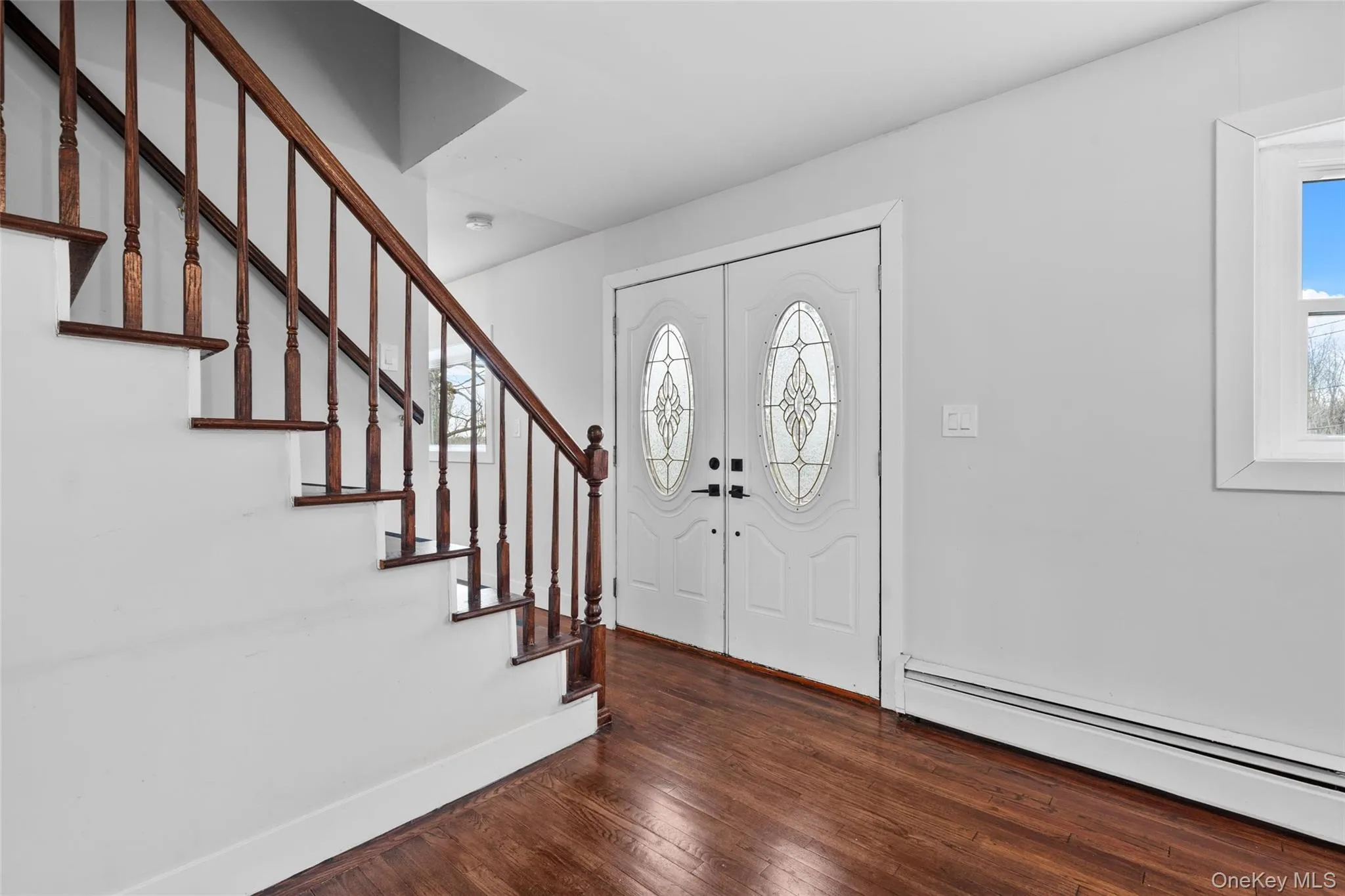 Foyer entrance with hardwood / wood-style flooring, stairway, baseboards, and baseboard heating Foyer entrance with hardwood / wood-style flooring, stairway, baseboards, and baseboard heating