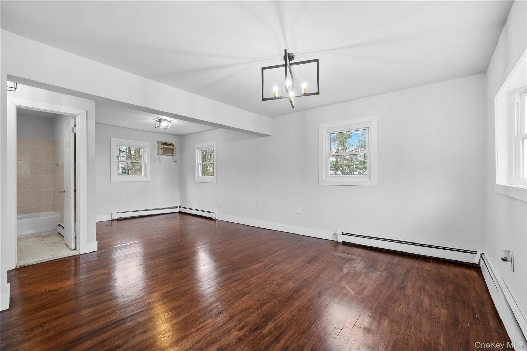 Unfurnished room with hardwood / wood-style flooring, a notable chandelier, and a baseboard radiator Unfurnished room with hardwood / wood-style flooring, a notable chandelier, and a baseboard radiator