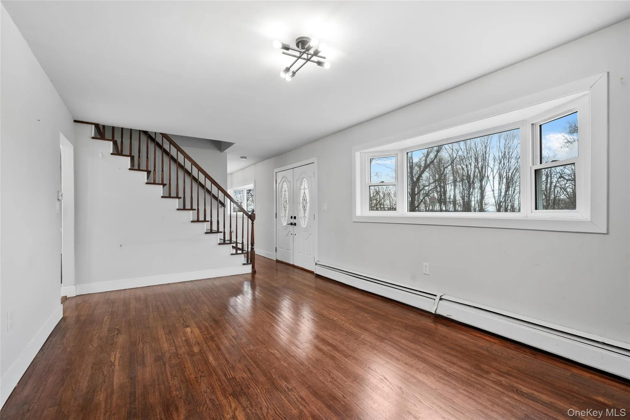 Entryway featuring baseboard heating, stairway, baseboards, and wood finished floors Entryway featuring baseboard heating, stairway, baseboards, and wood finished floors