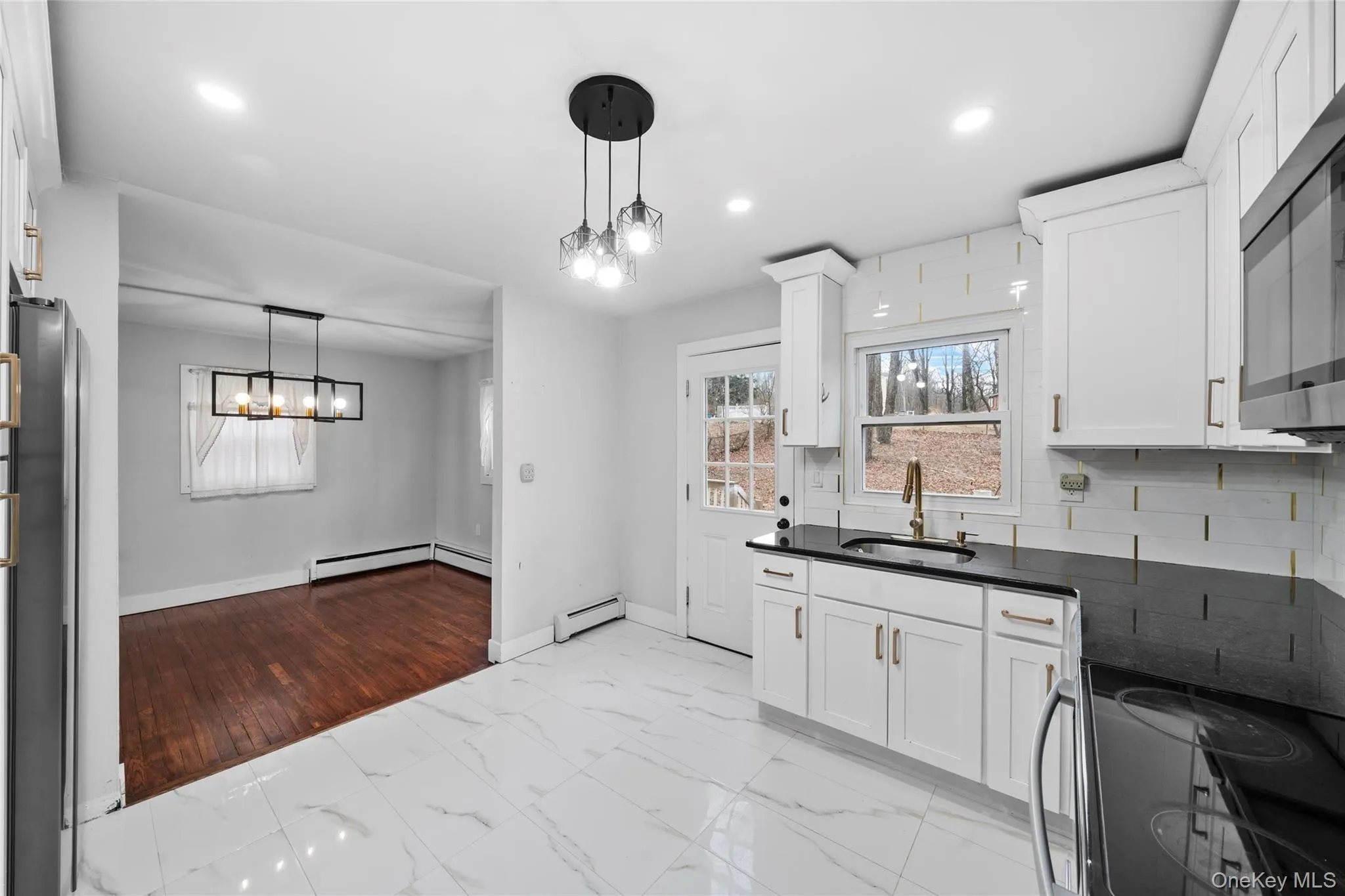 Kitchen featuring dark countertops, a baseboard heating unit, marble finish floor, stainless steel appliances, and a sink Kitchen featuring dark countertops, a baseboard heating unit, marble finish floor, stainless steel appliances, and a sink