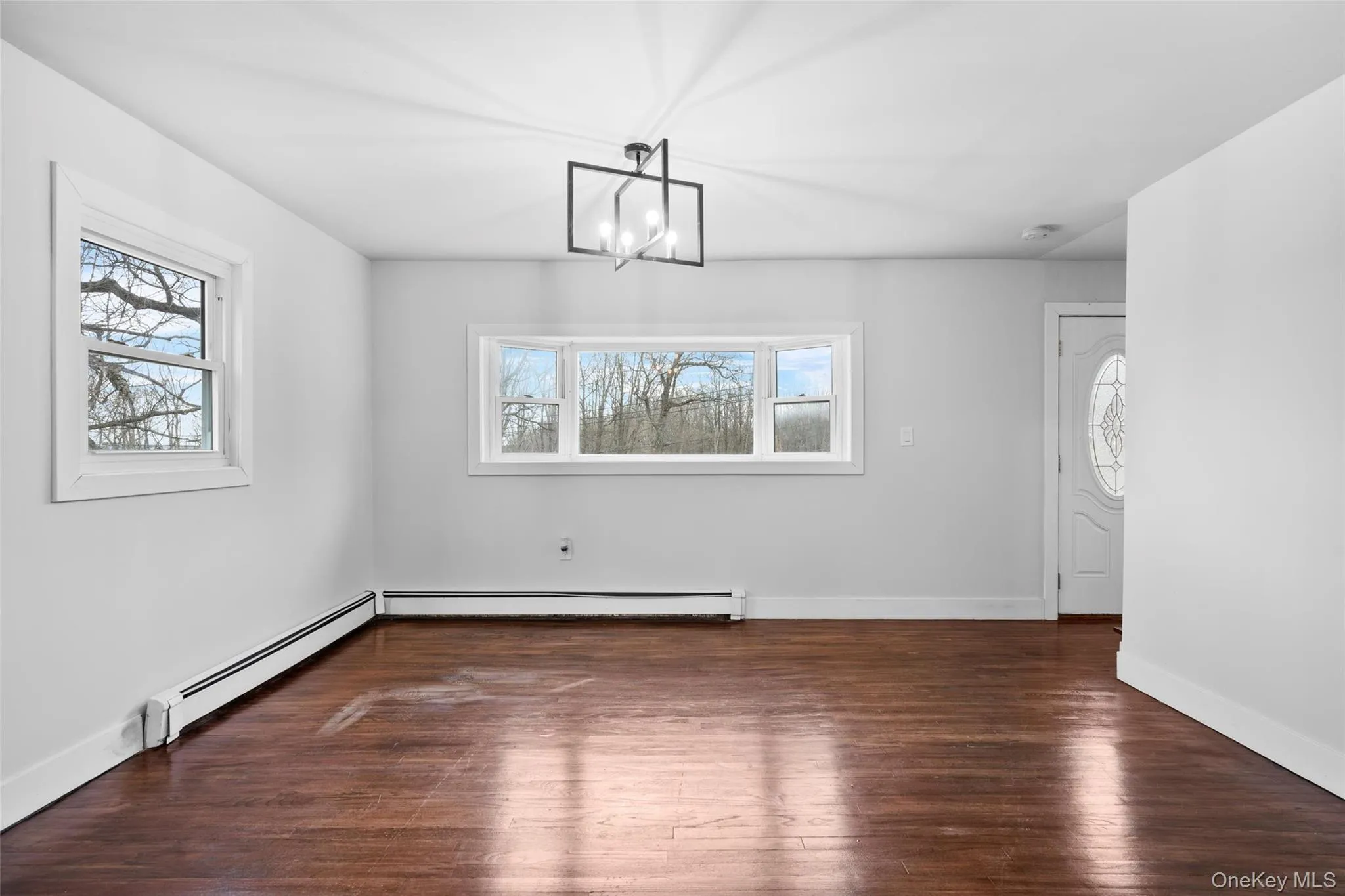 Unfurnished dining area featuring baseboard heating, baseboards, an inviting chandelier, and wood finished floors Unfurnished dining area featuring baseboard heating, baseboards, an inviting chandelier, and wood finished floors