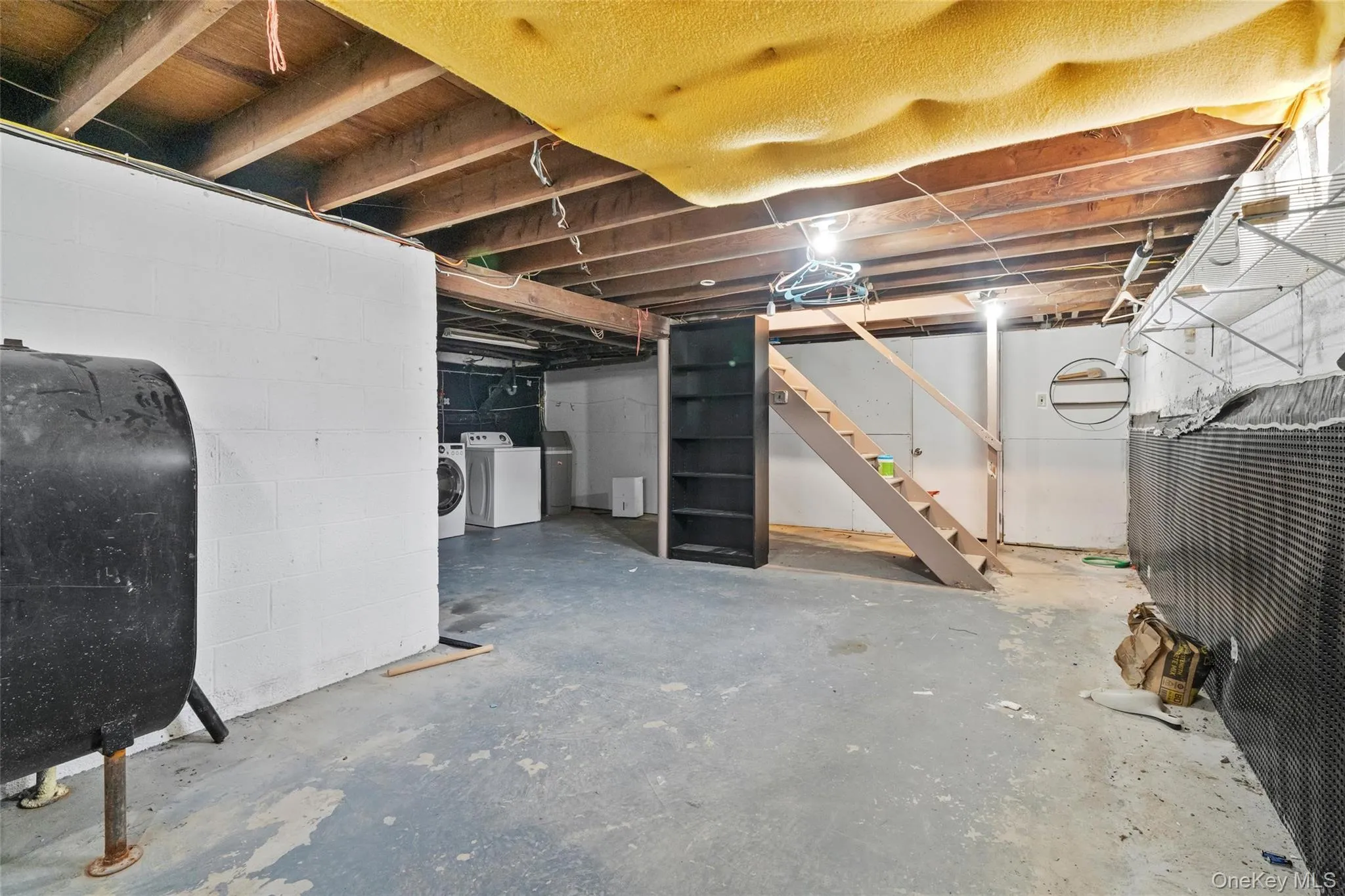 Unfinished below grade area with washing machine and dryer, stairs, heating fuel, and concrete block wall Unfinished below grade area with washing machine and dryer, stairs, heating fuel, and concrete block wall