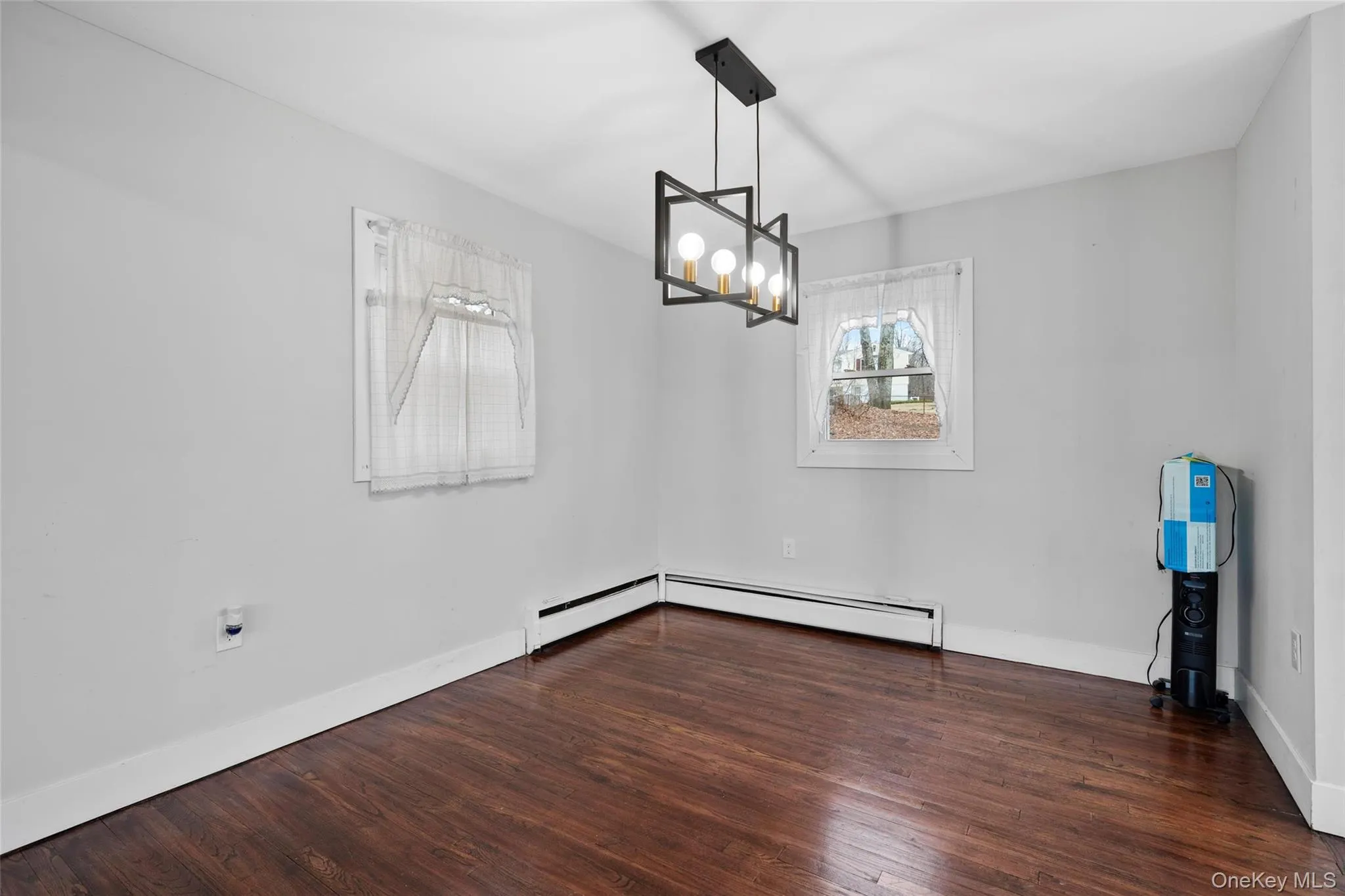 Empty room featuring baseboards, a notable chandelier, baseboard heating, and wood finished floors Empty room featuring baseboards, a notable chandelier, baseboard heating, and wood finished floors