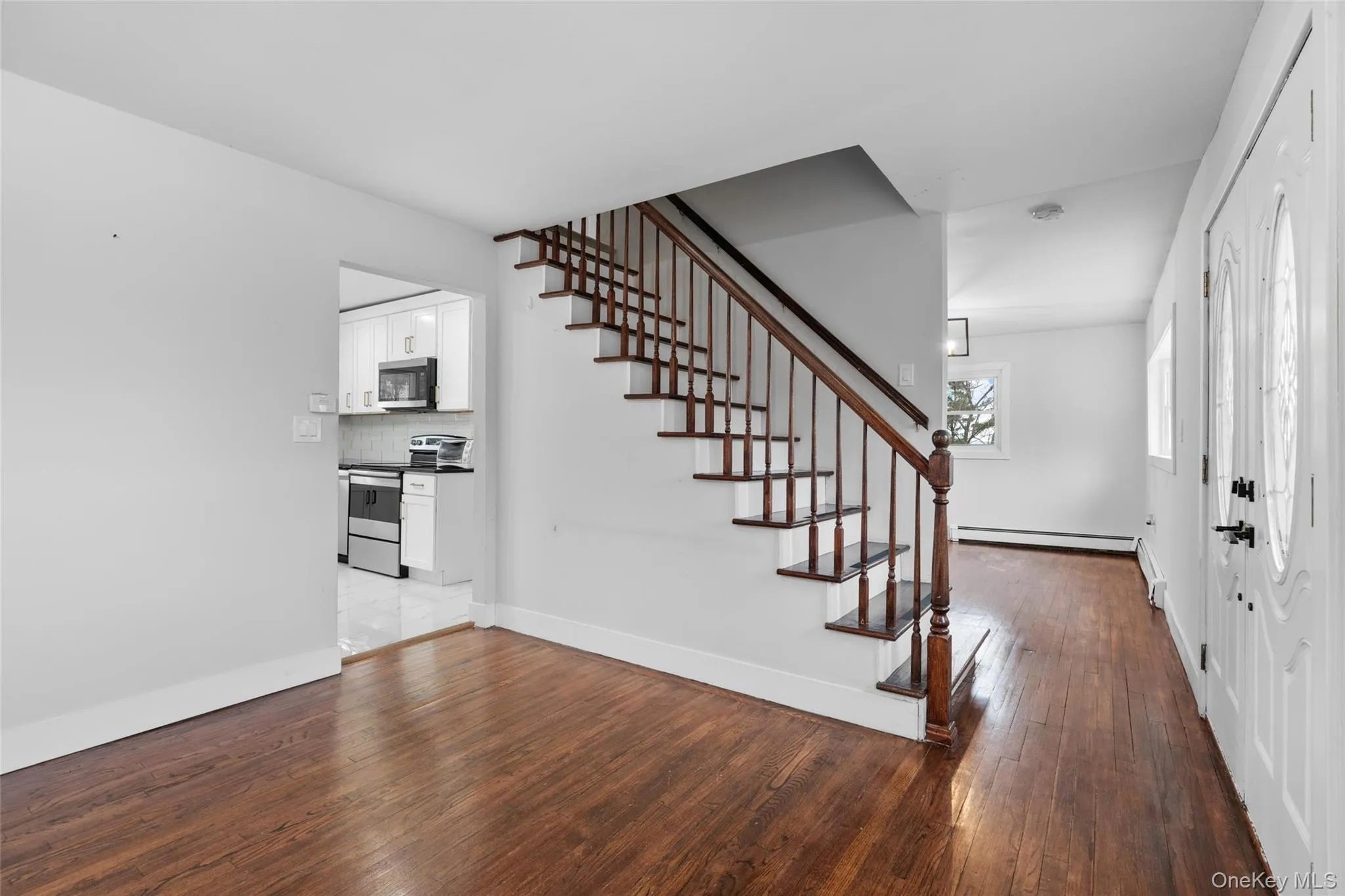 Foyer entrance featuring stairway, wood-type flooring, baseboard heating, and baseboards Foyer entrance featuring stairway, wood-type flooring, baseboard heating, and baseboards