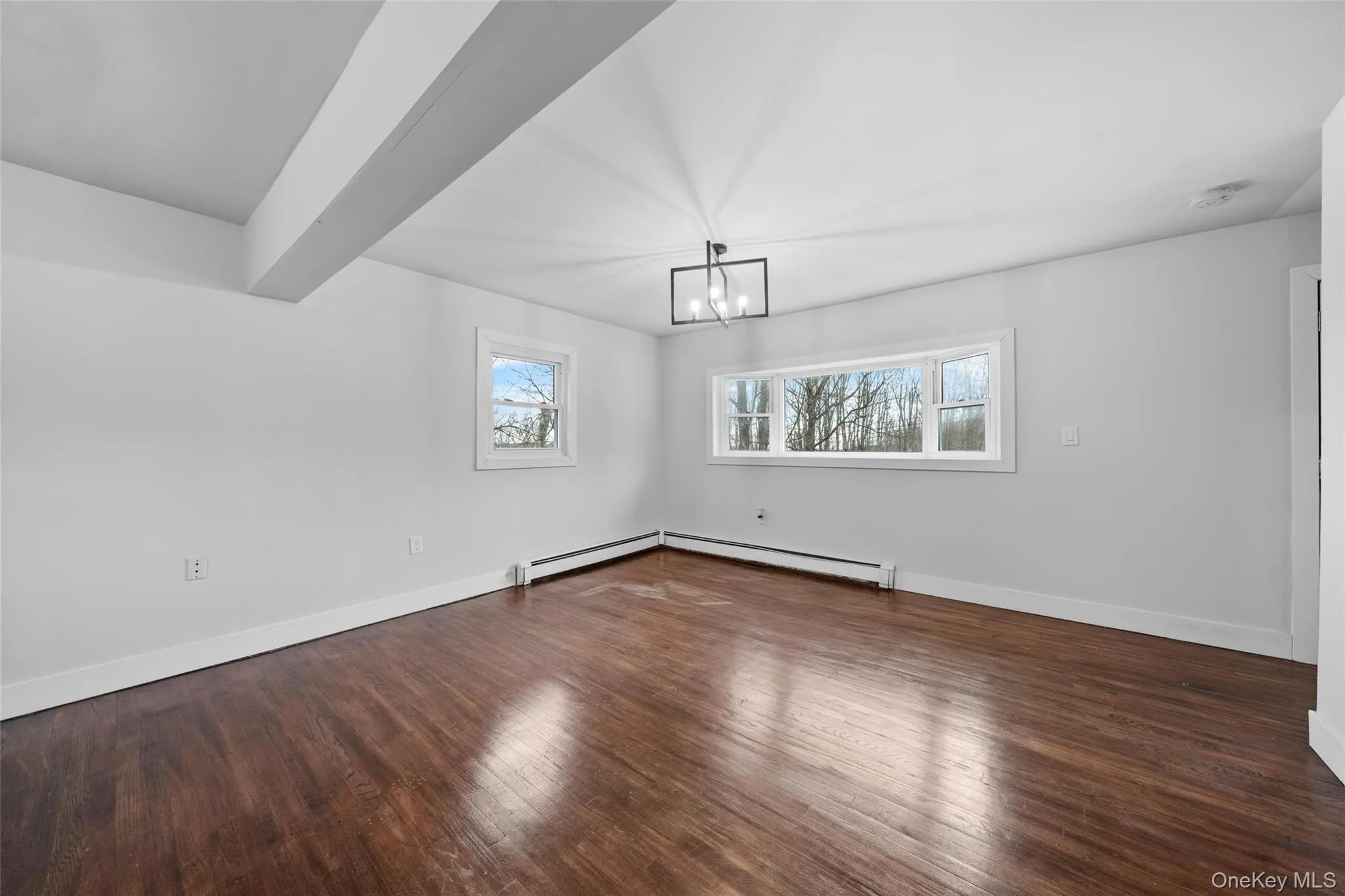 Empty room featuring a notable chandelier, baseboards, and wood finished floors Empty room featuring a notable chandelier, baseboards, and wood finished floors