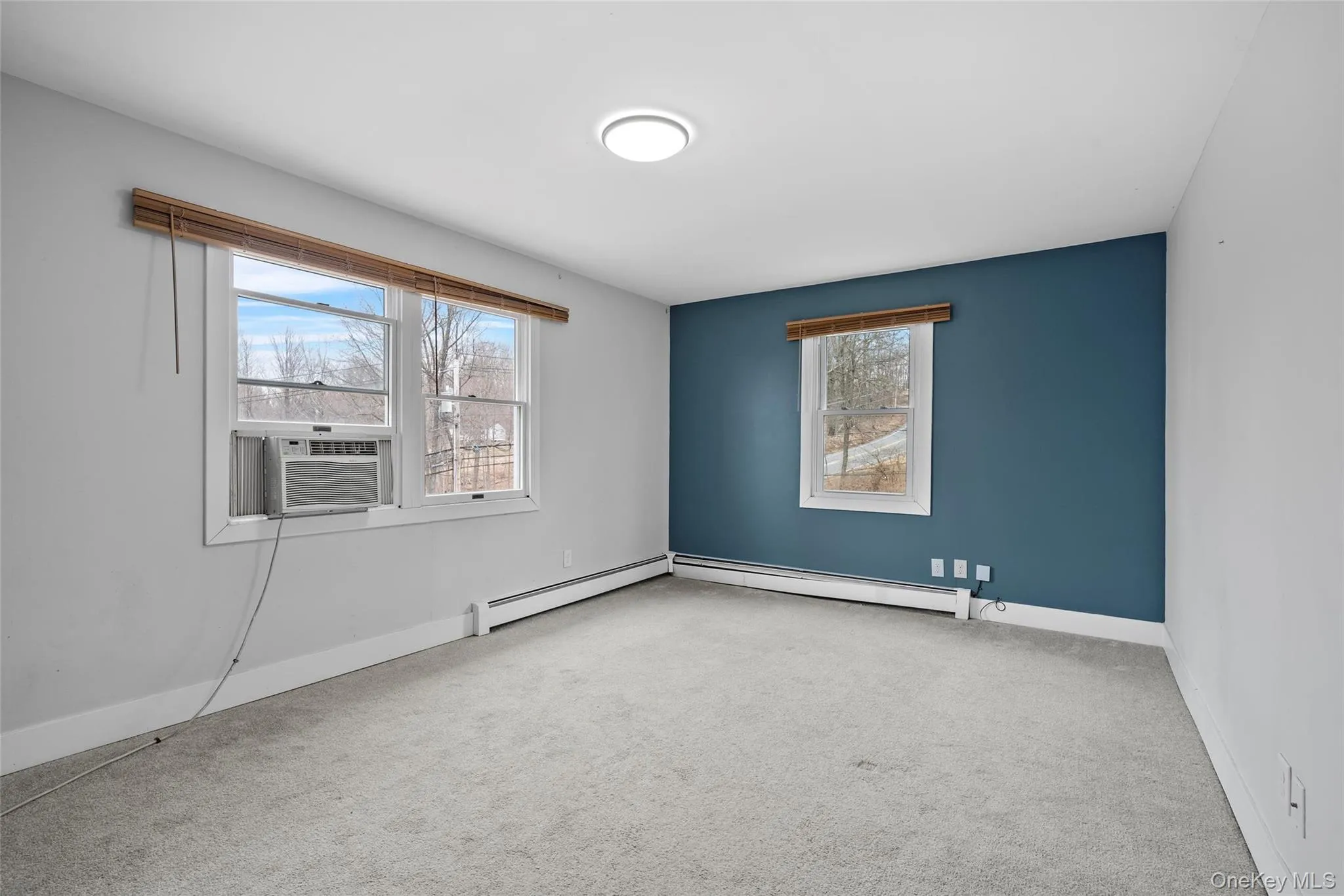 Carpeted empty room with cooling unit, baseboards, and a baseboard radiator Carpeted empty room with cooling unit, baseboards, and a baseboard radiator