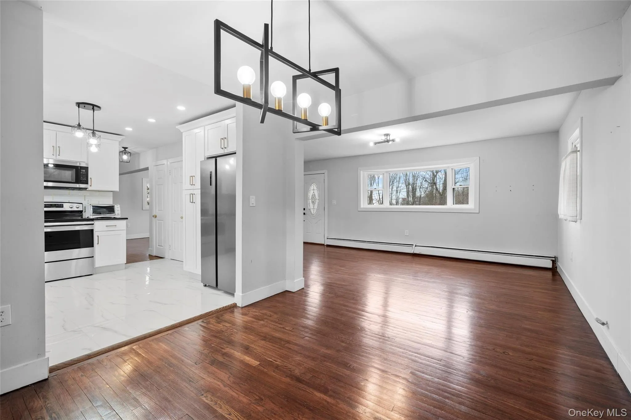 Kitchen featuring a baseboard heating unit, a notable chandelier, appliances with stainless steel finishes, and open floor plan Kitchen featuring a baseboard heating unit, a notable chandelier, appliances with stainless steel finishes, and open floor plan