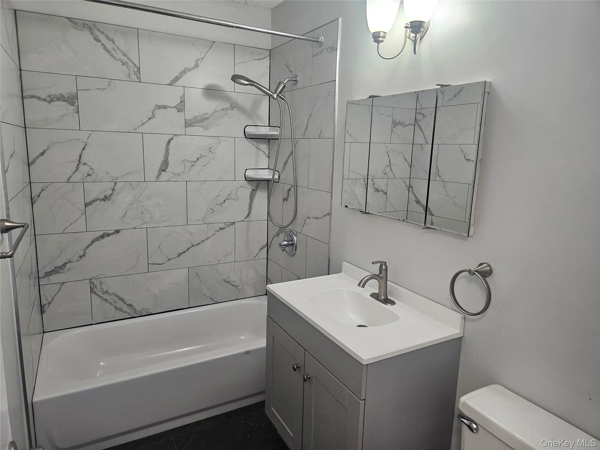 Bathroom featuring a white subway tile tub surround, white bathtub, a gray vanity with an integrated sink, a mirrored medicine cabinet, and brushed nickel fixtures Bathroom featuring a white subway tile tub surround, white bathtub, a gray vanity with an integrated sink, a mirrored medicine cabinet, and brushed nickel fixtures