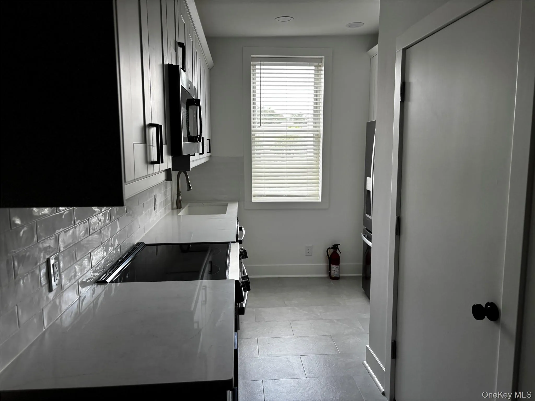 Kitchen featuring stainless steel microwave, tasteful backsplash, light tile patterned floors, light countertops, and range with electric stovetop Kitchen featuring stainless steel microwave, tasteful backsplash, light tile patterned floors, light countertops, and range with electric stovetop