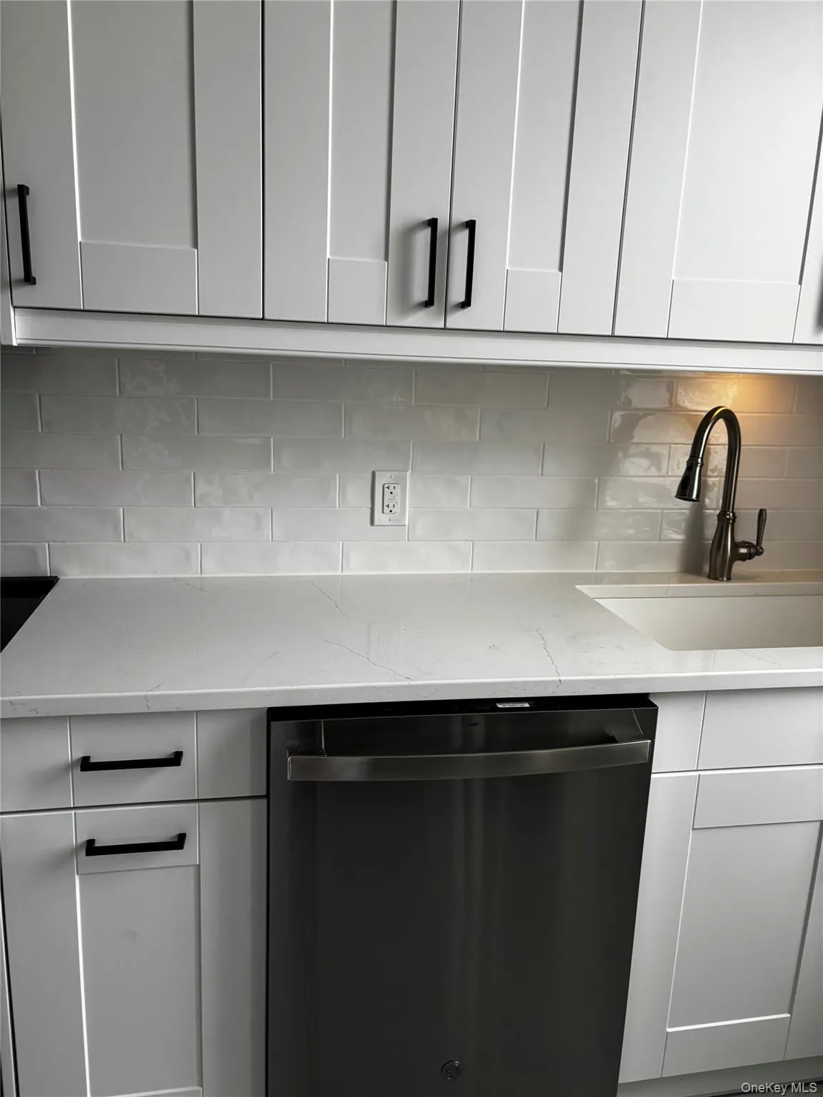 Kitchen featuring dishwashing machine, tasteful backsplash, light stone counters, and white cabinetry Kitchen featuring dishwashing machine, tasteful backsplash, light stone counters, and white cabinetry