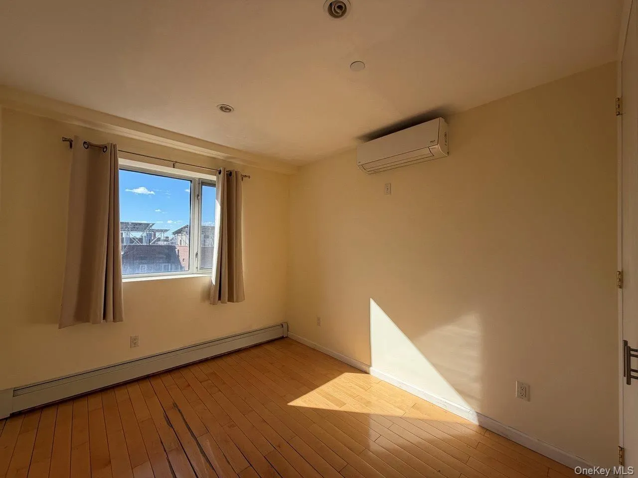 Bright room featuring wood-finish flooring, a window with an exterior outlook, an installed split-unit air conditioning system, and recessed ceiling lighting Bright room featuring wood-finish flooring, a window with an exterior outlook, an installed split-unit air conditioning system, and recessed ceiling lighting