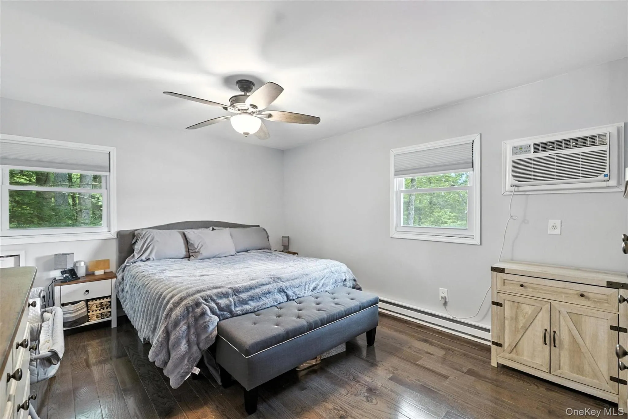 Bedroom with a baseboard radiator, dark wood-style flooring, a wall unit AC, and ceiling fan Bedroom with a baseboard radiator, dark wood-style flooring, a wall unit AC, and ceiling fan