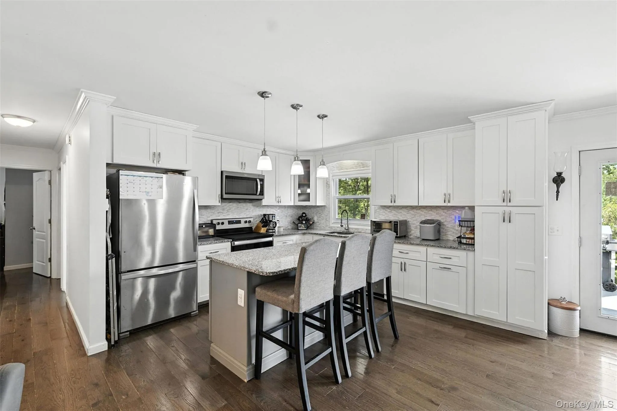 Kitchen featuring appliances with stainless steel finishes, crown molding, white cabinets, backsplash, and dark wood-style floors Kitchen featuring appliances with stainless steel finishes, crown molding, white cabinets, backsplash, and dark wood-style floors