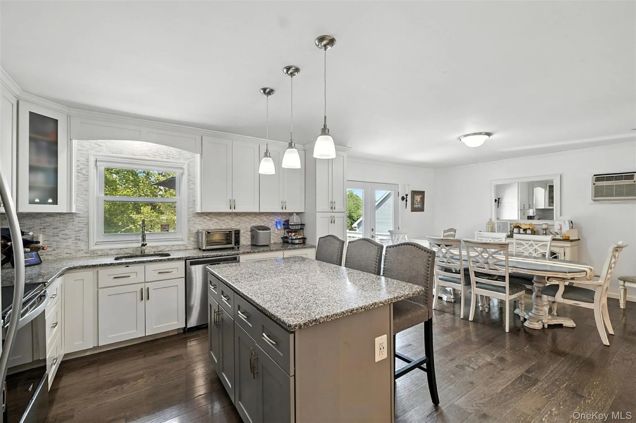 Kitchen with a kitchen breakfast bar, dark wood finished floors, backsplash, and white cabinets Kitchen with a kitchen breakfast bar, dark wood finished floors, backsplash, and white cabinets